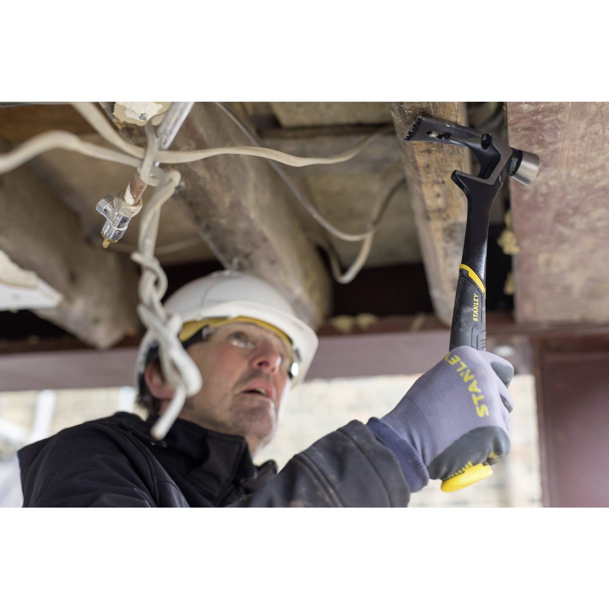 A person wearing a hard hat is working with a hammer on a wooden ceiling. Construction site in the background.