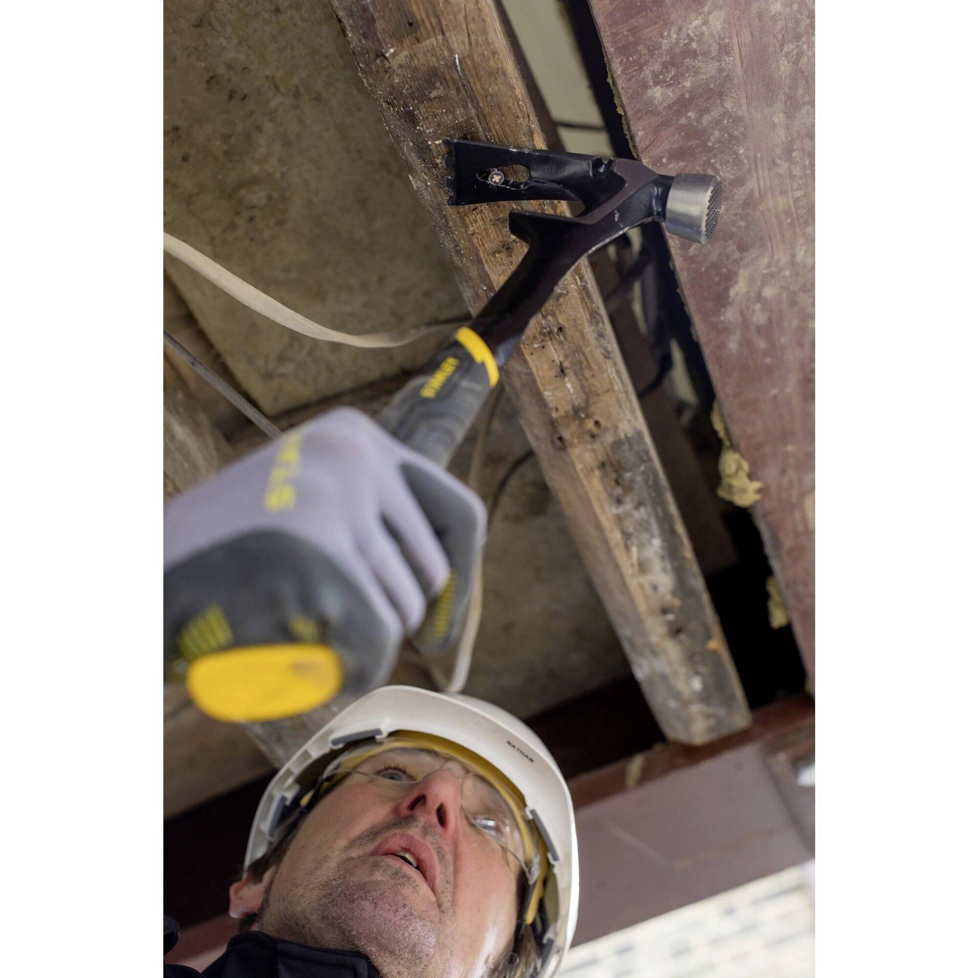 A person wearing a safety helmet and gloves is using a hammer to secure a beam in a ceiling.