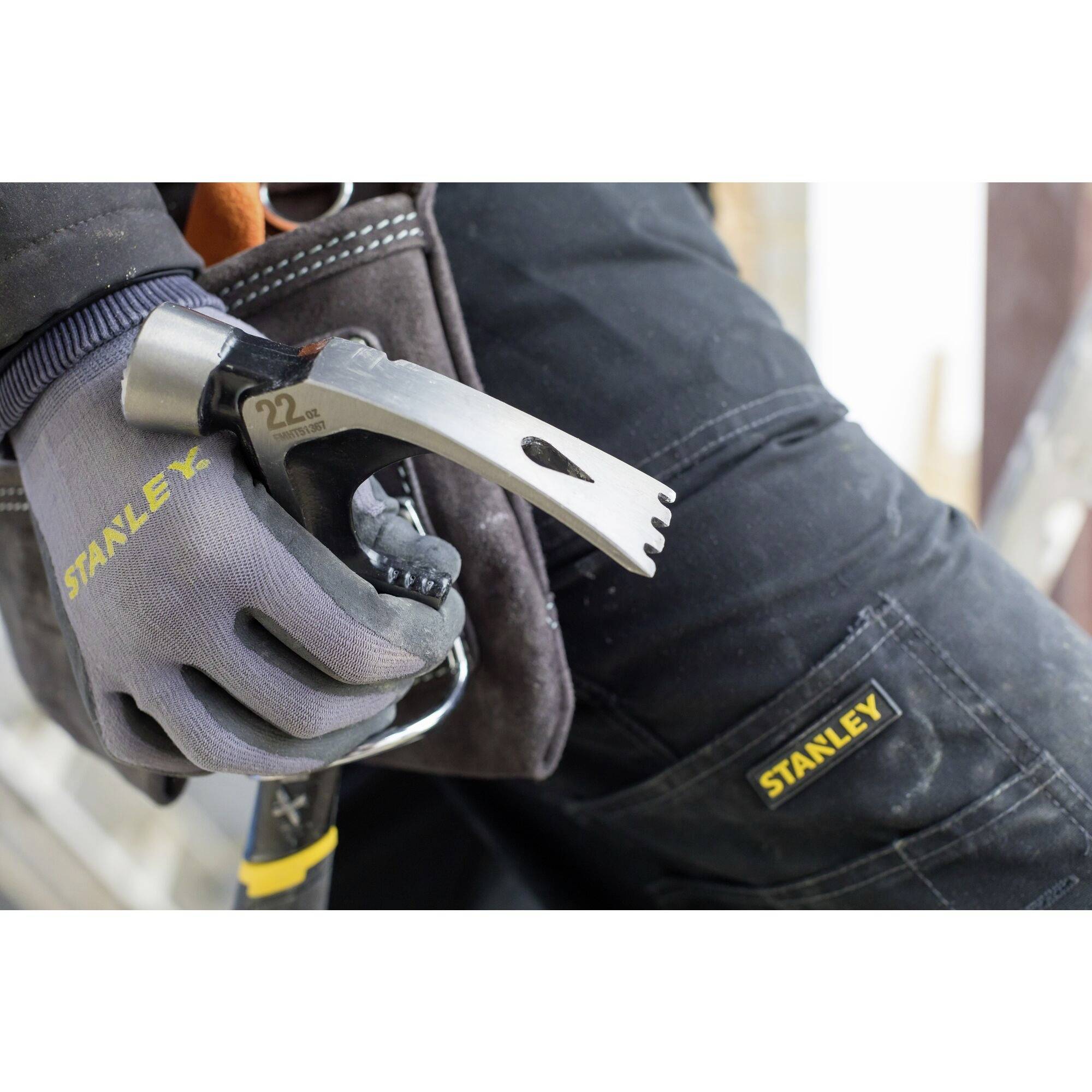 A person wearing a Stanley work glove is holding a hammer. The glove and clothing are branded with 'Stanley'. Focus on the tool and brand.