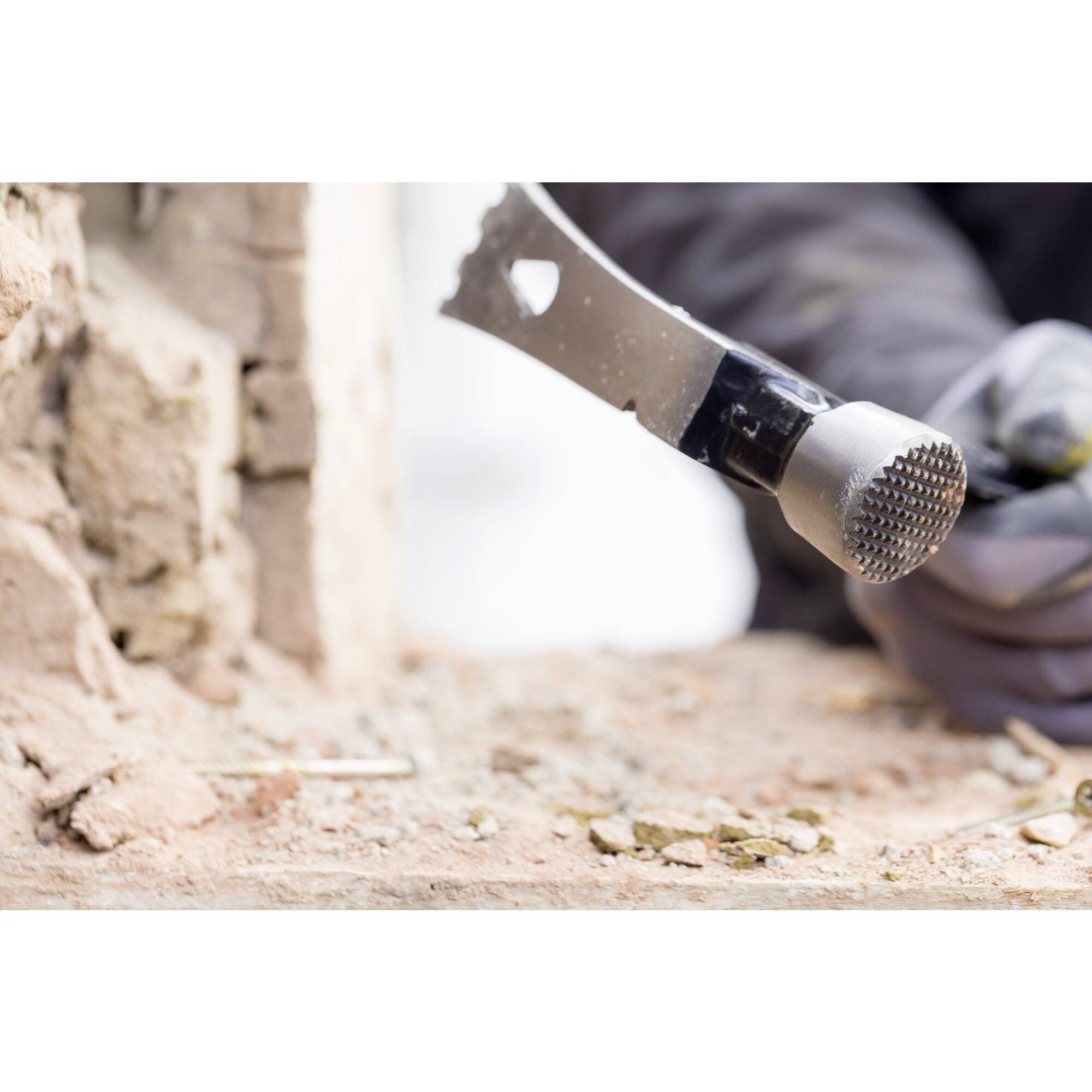 A person is removing mortar with a hammer tool from a stone wall. The person is wearing grey gloves.