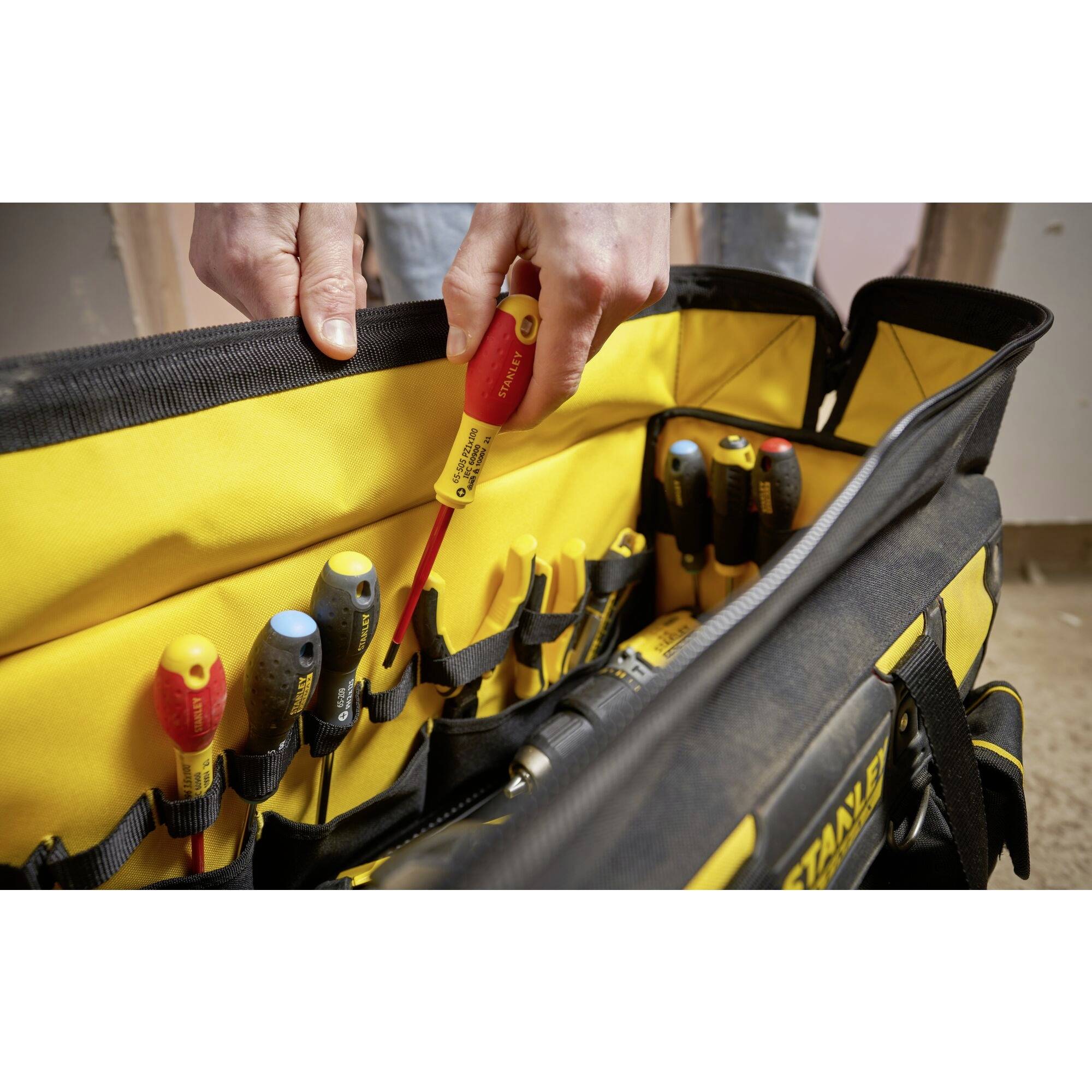 A hand pulls out a screwdriver from a yellow tool bag filled with various screwdrivers.