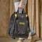 A person is wearing a black 'Stanley Fatmax' tool rucksack adorned with a golden logo. Wooden boards are visible in the background.
