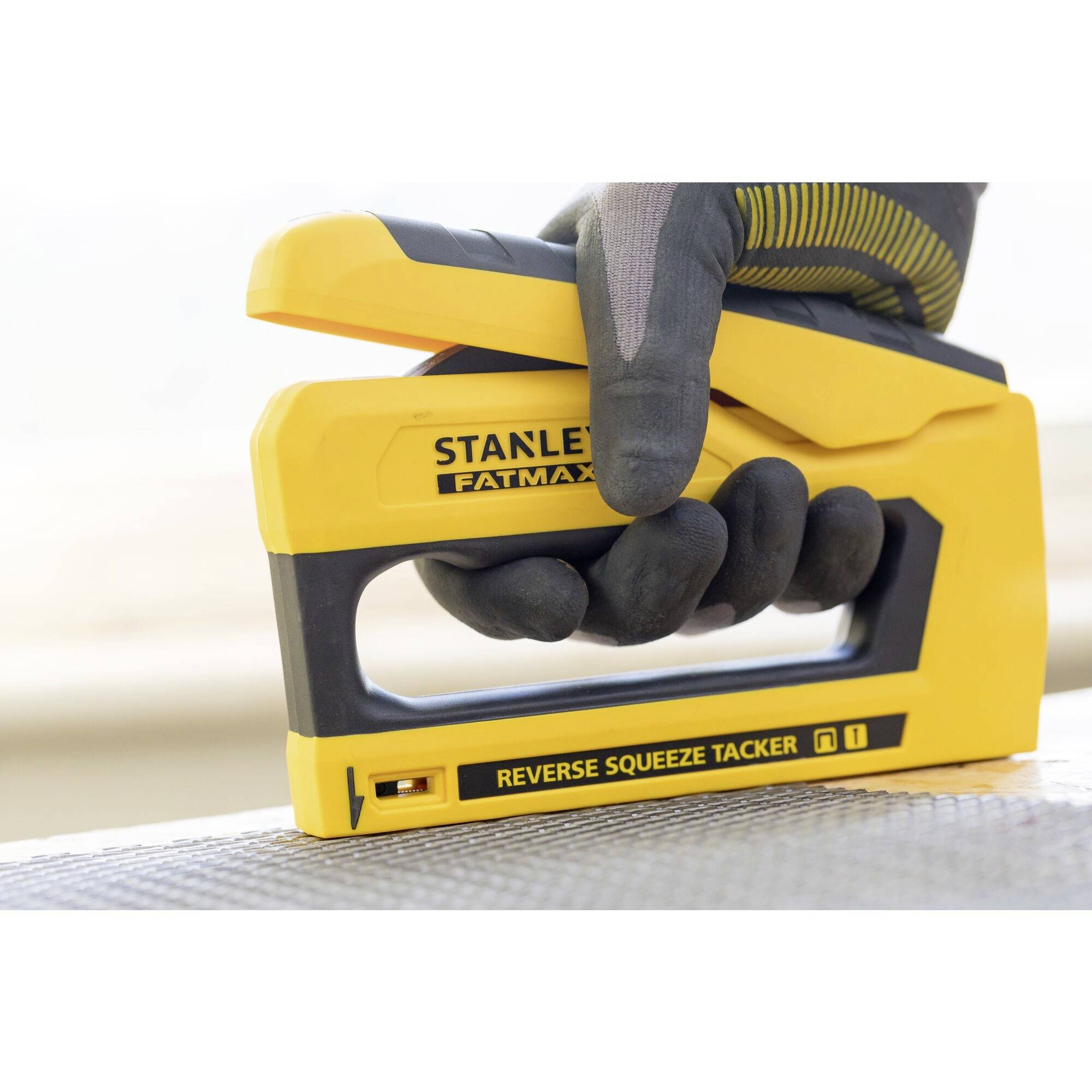 Yellow hand stapler, manually pressed, with the inscription 'Stanley Fatmax Reverse Squeeze Tacker' on a textured surface.