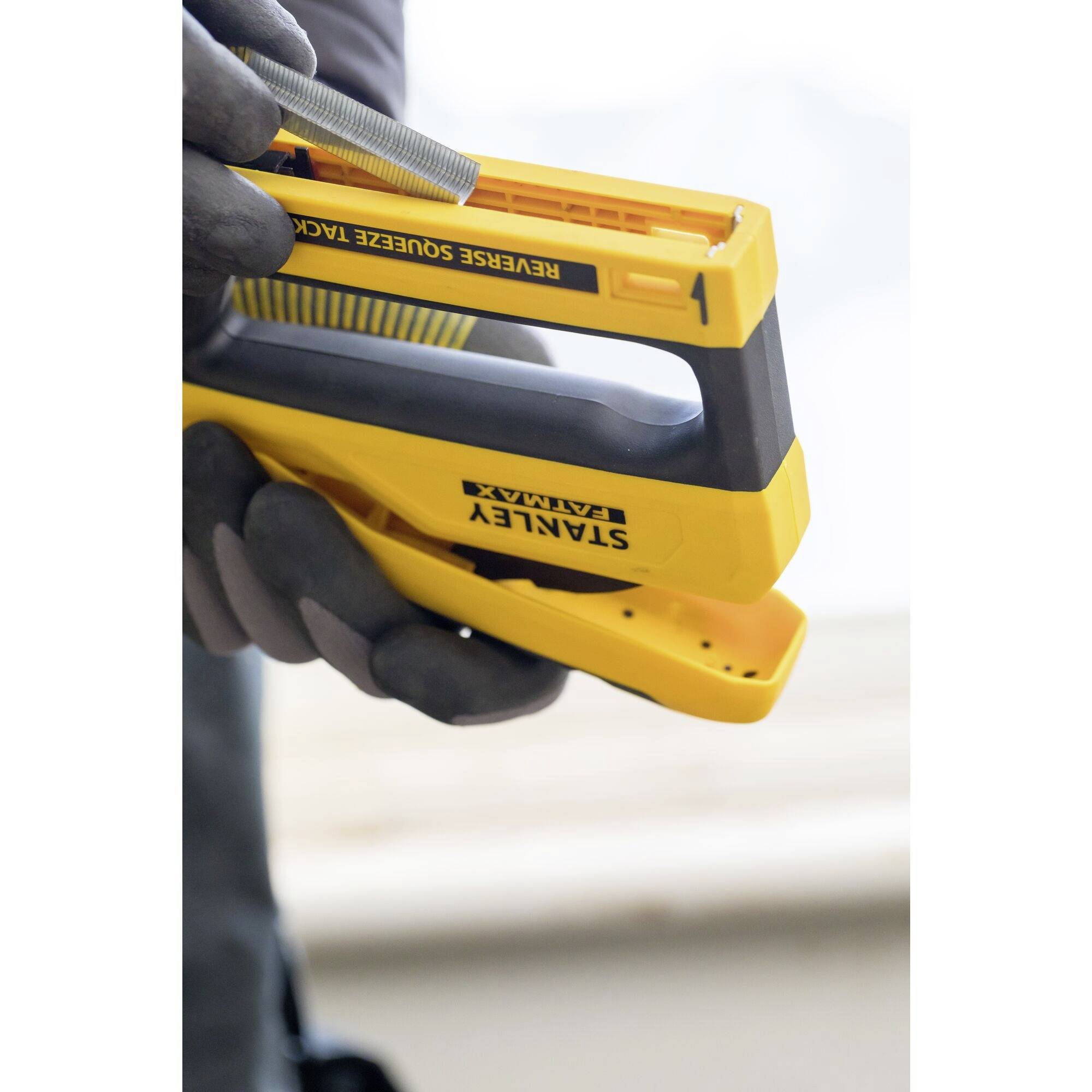 A person is holding a yellow hand stapler, ready for use. The focus is on the device used for DIY or craftwork.
