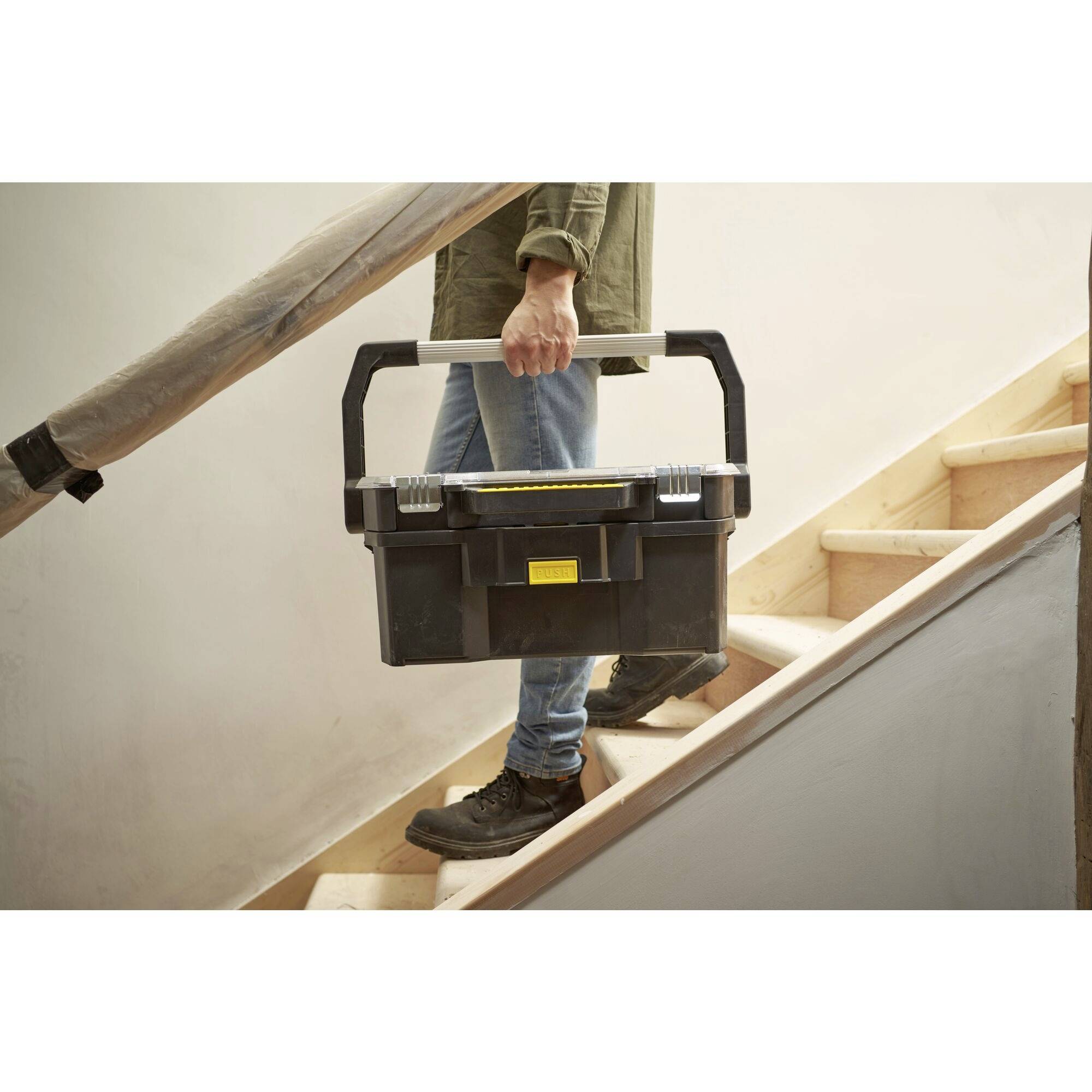 A person is carrying a black toolbox down a staircase. They are holding the box by the white handle with both hands.