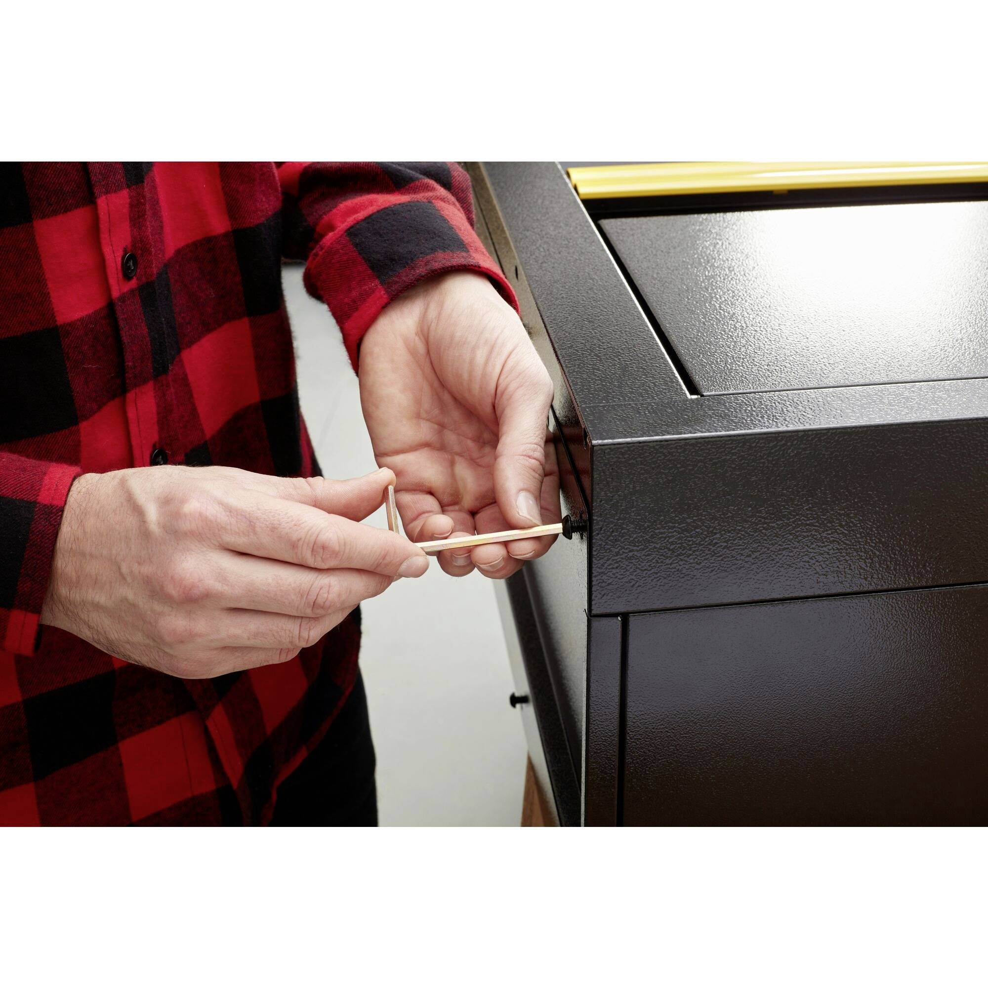 A person is wearing a red and black checked shirt and using a screwdriver to tighten a screw in a metal device.