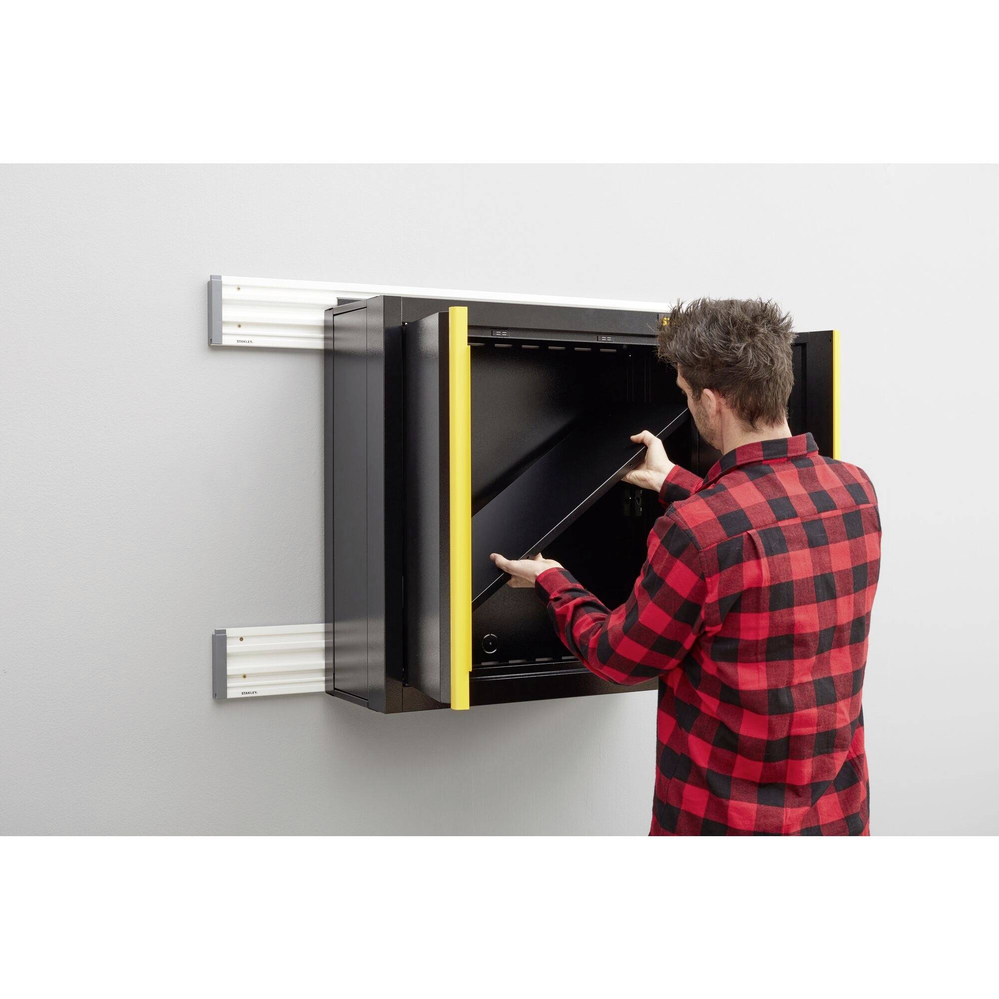 A person in a checked shirt pulls a black screen from a structured wall mechanism.