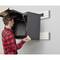 A man is installing a black tool cabinet on a wall. The cabinet is positioned at a height and is open.