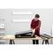 A man in a lumberjack shirt is assembling a metal shelving unit on a table. A ladder is standing in the background.