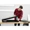 A man in a red and black checked shirt is assembling a black metal frame on a wooden table, using tools.
