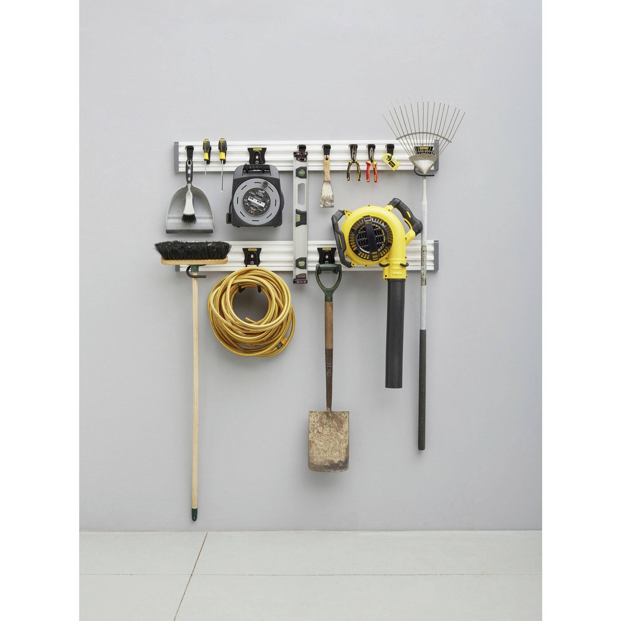 Organised garden tools on a wall mount: broom, hose, spade, leaf blower and rake. Ideal for space-saving storage.
