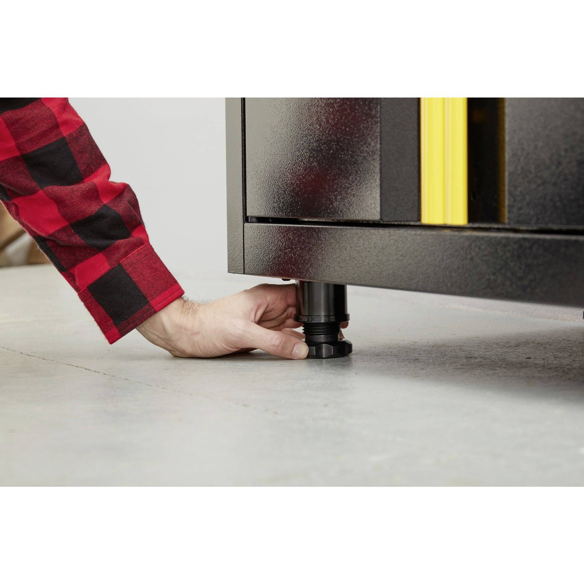 'A man in checked clothing adjusts an adjustable furniture foot on a black shelving unit.'