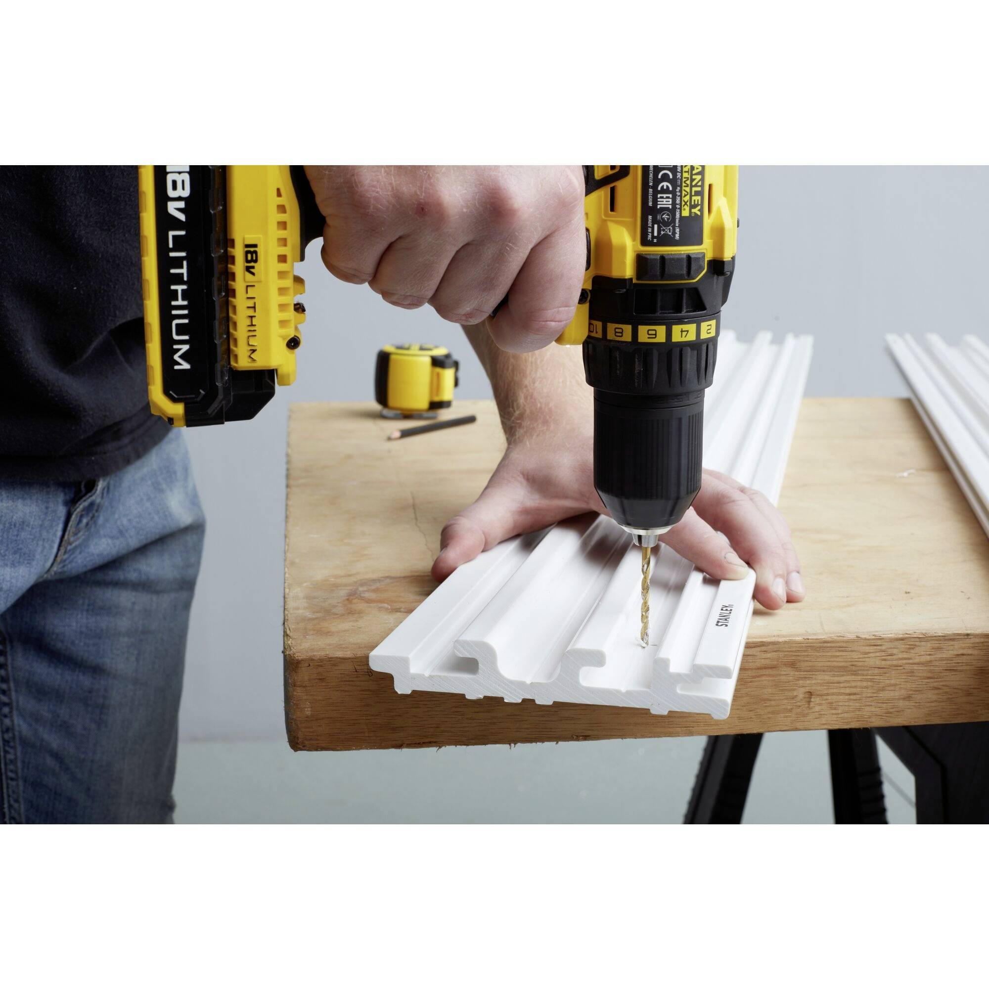 'Image of a person drilling a hole in a white plastic component with a cordless drill on a workbench with a measuring tape.'