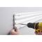 A person is securing a white plastic strip to a grey wall using a yellow cordless drill.