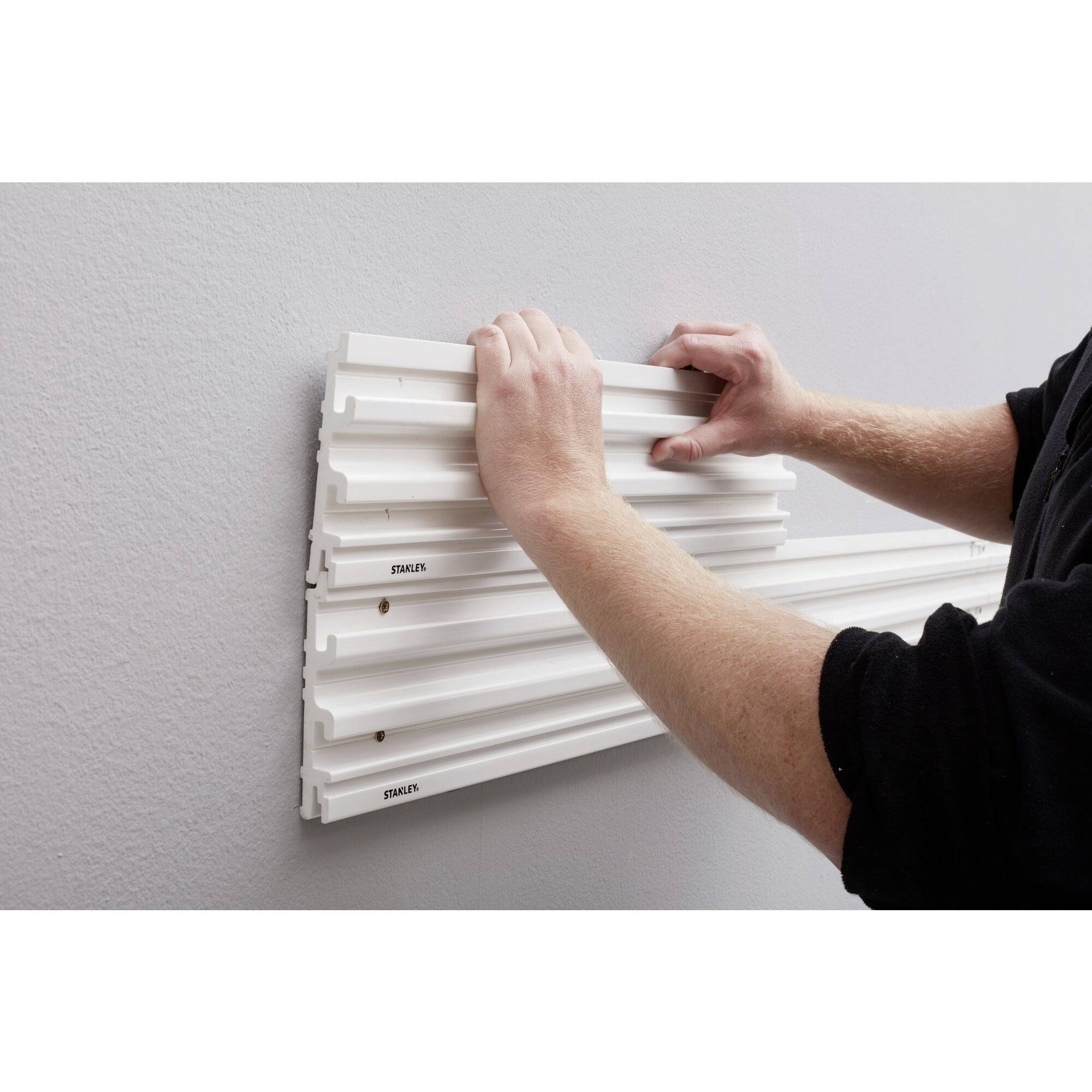 A person is mounting a white wall panel on a grey wall by aligning it with both hands.