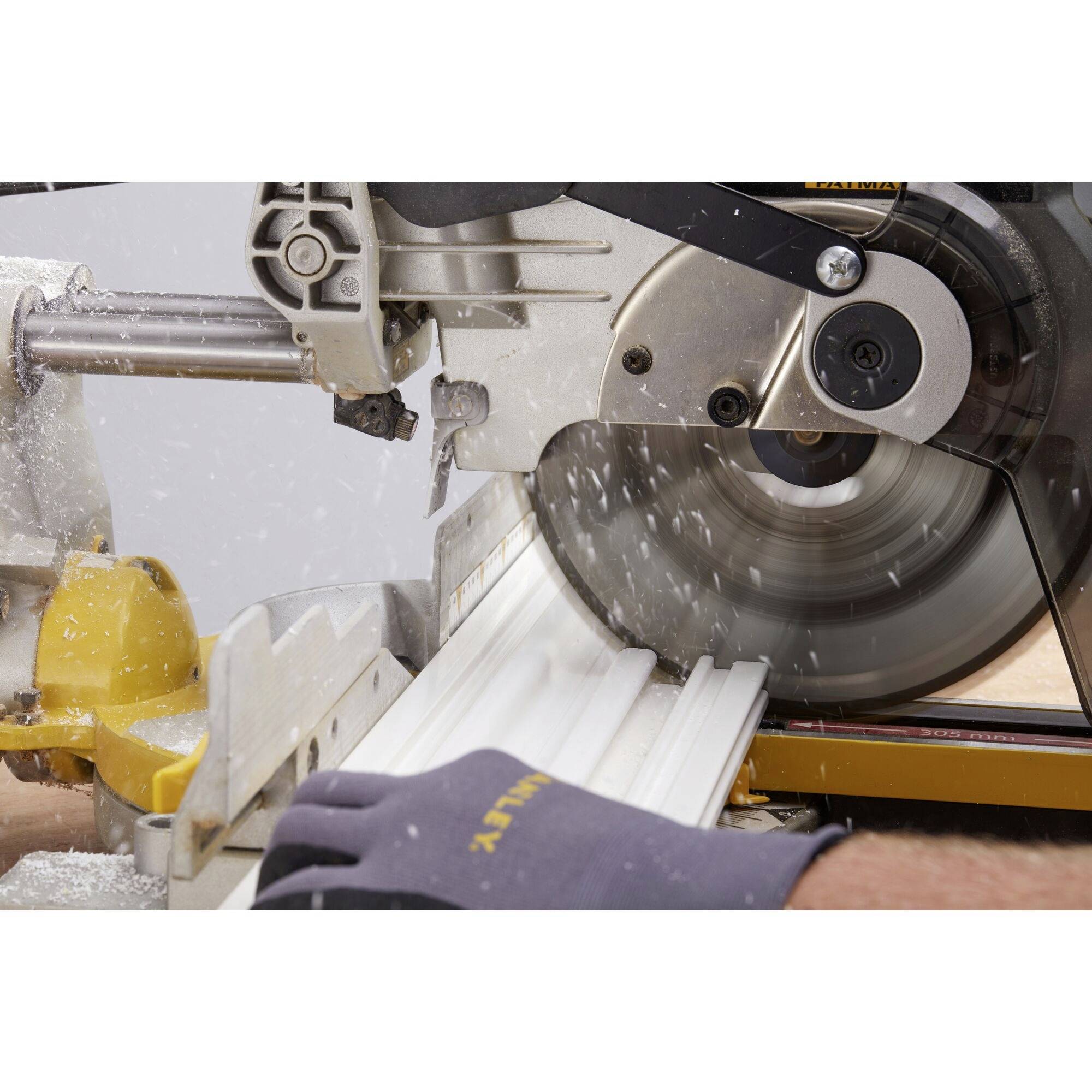 A chop saw precisely cuts a white piece of wood. Sparks fly and a person holds the wood with a gloved hand.