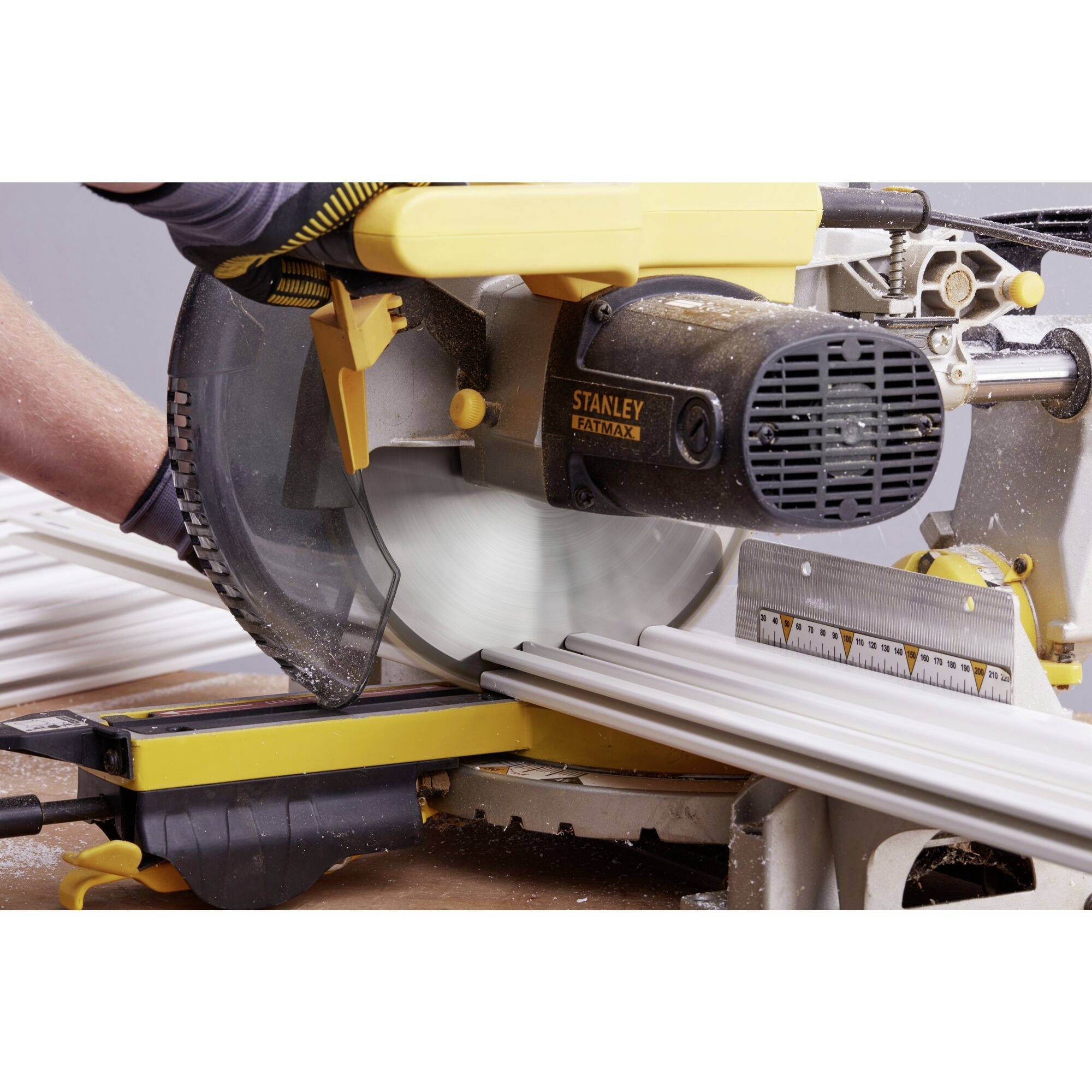 A person is cutting a long white board with an electrically powered mitre saw. The saw is black and yellow.