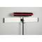 A red broom with bristles is attached to a black handle and hangs from a white bracket on the wall.