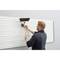 A person in work attire is using a broom to clean a radiator cover on the wall.