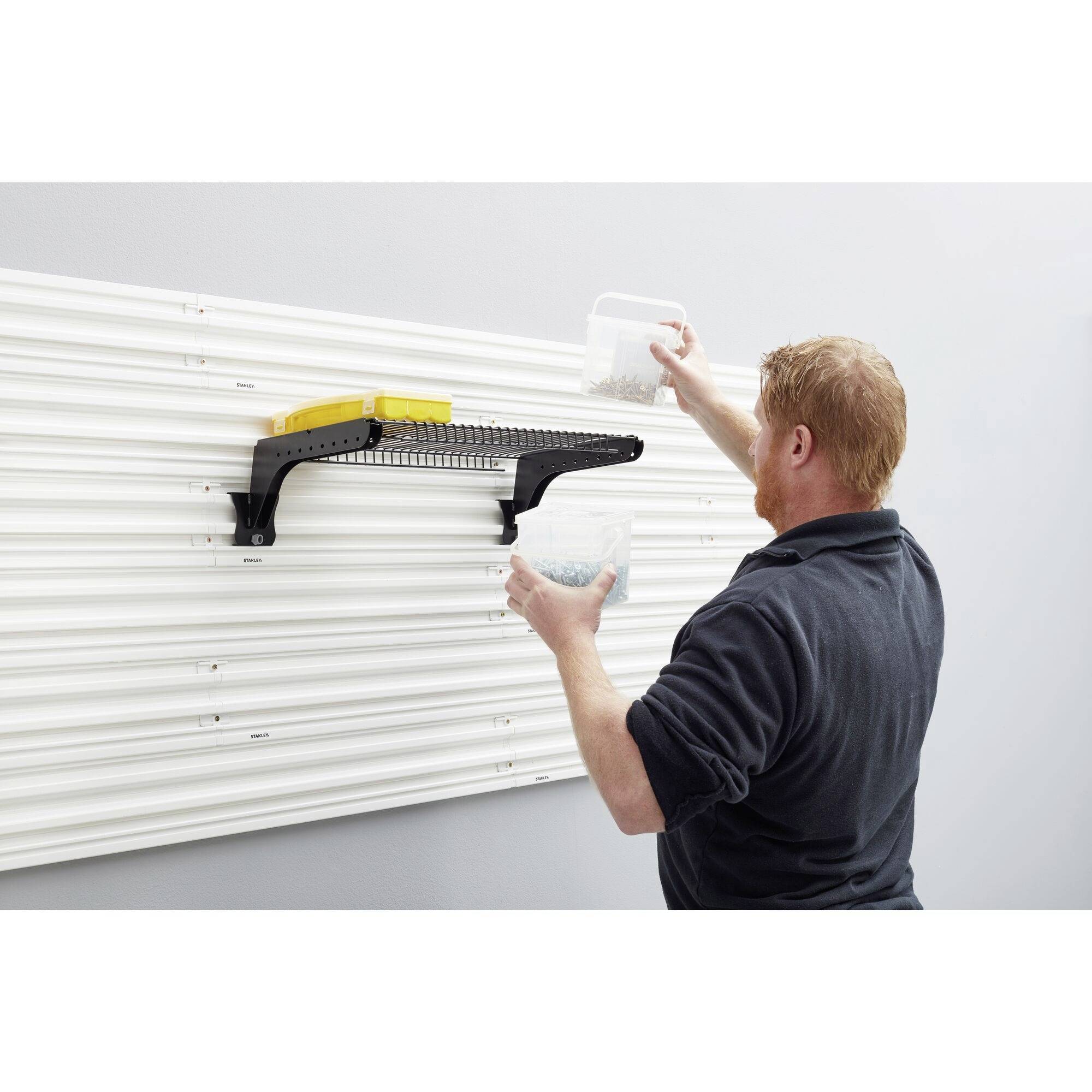 A person is fixing a shelf to a wall using a hook system and placing items on it.
