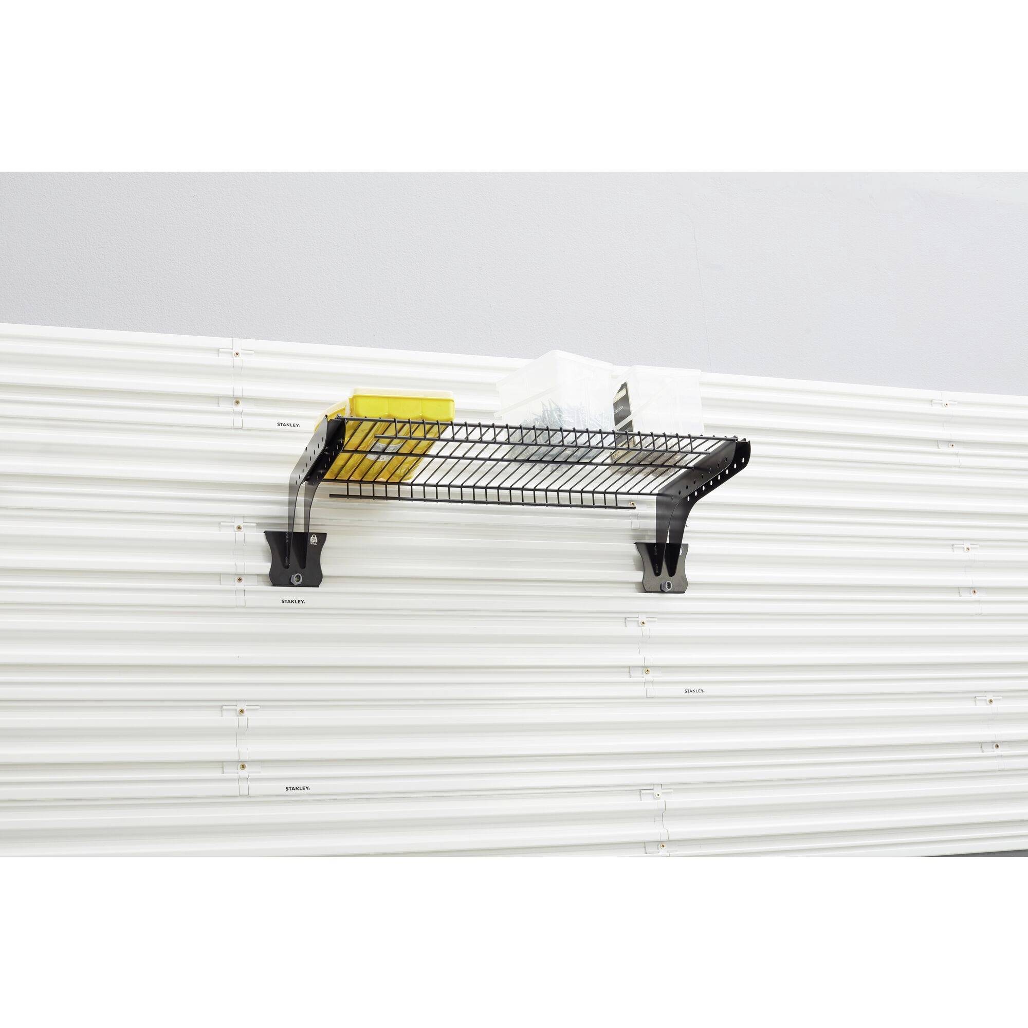 A single black metal shelving unit is mounted on a white wall. Yellow and blue items are placed on the shelf.