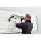A person is installing a black metal shelving unit on a white wall with horizontal grooves.
