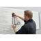 A man is securing a metal bracket to a vertical slatted wall in a bright room.