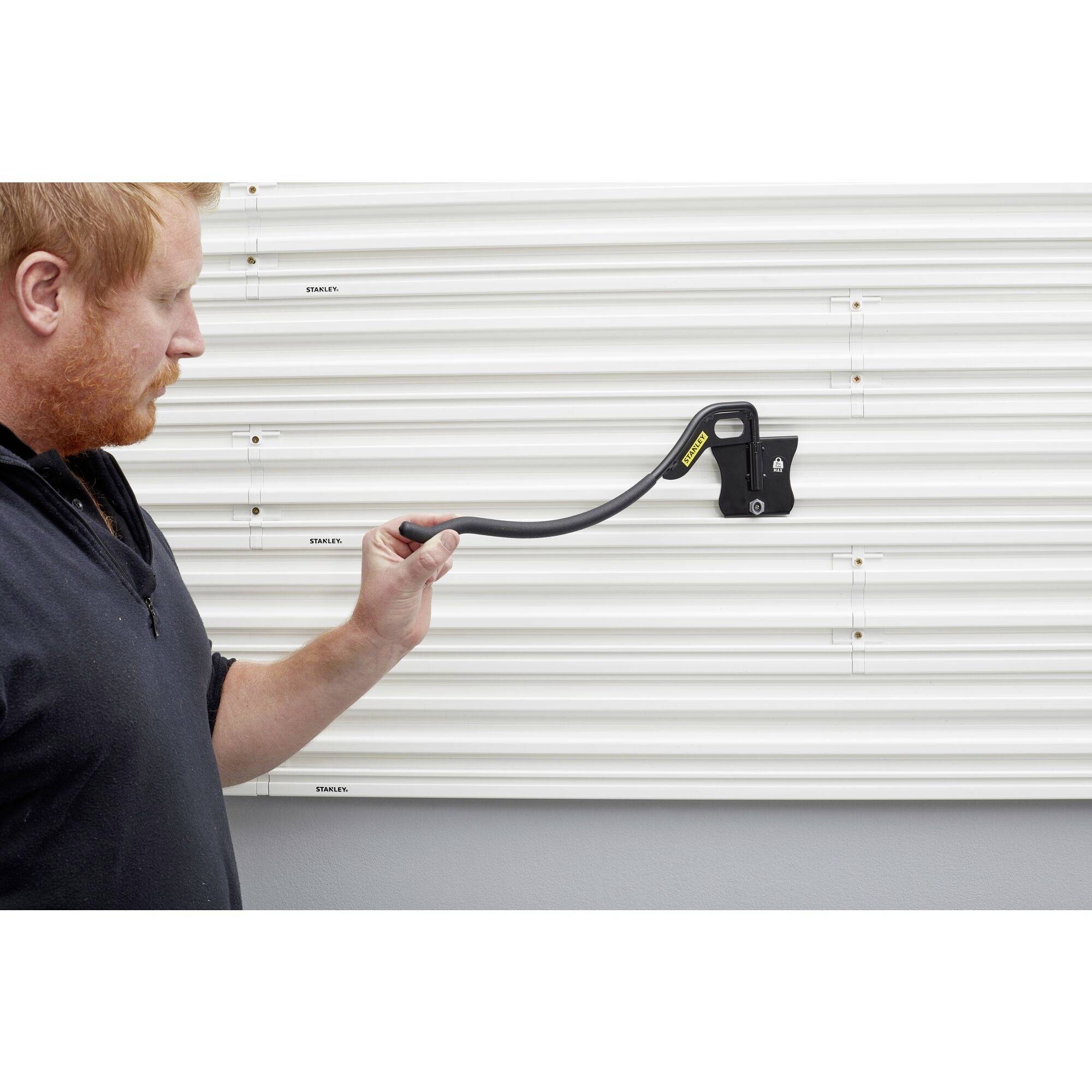A man is holding a device to measure resistance on a wall with metal panels. The device displays a digital reading.