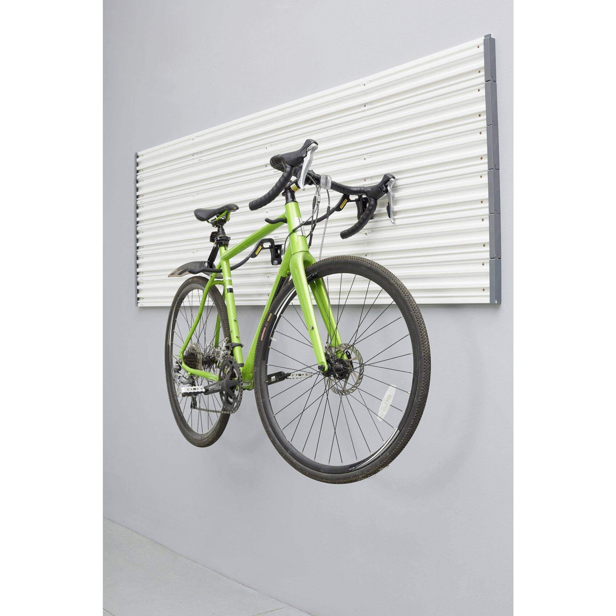 A green bicycle is suspended vertically on a white ribbed wall mount in a modern room.