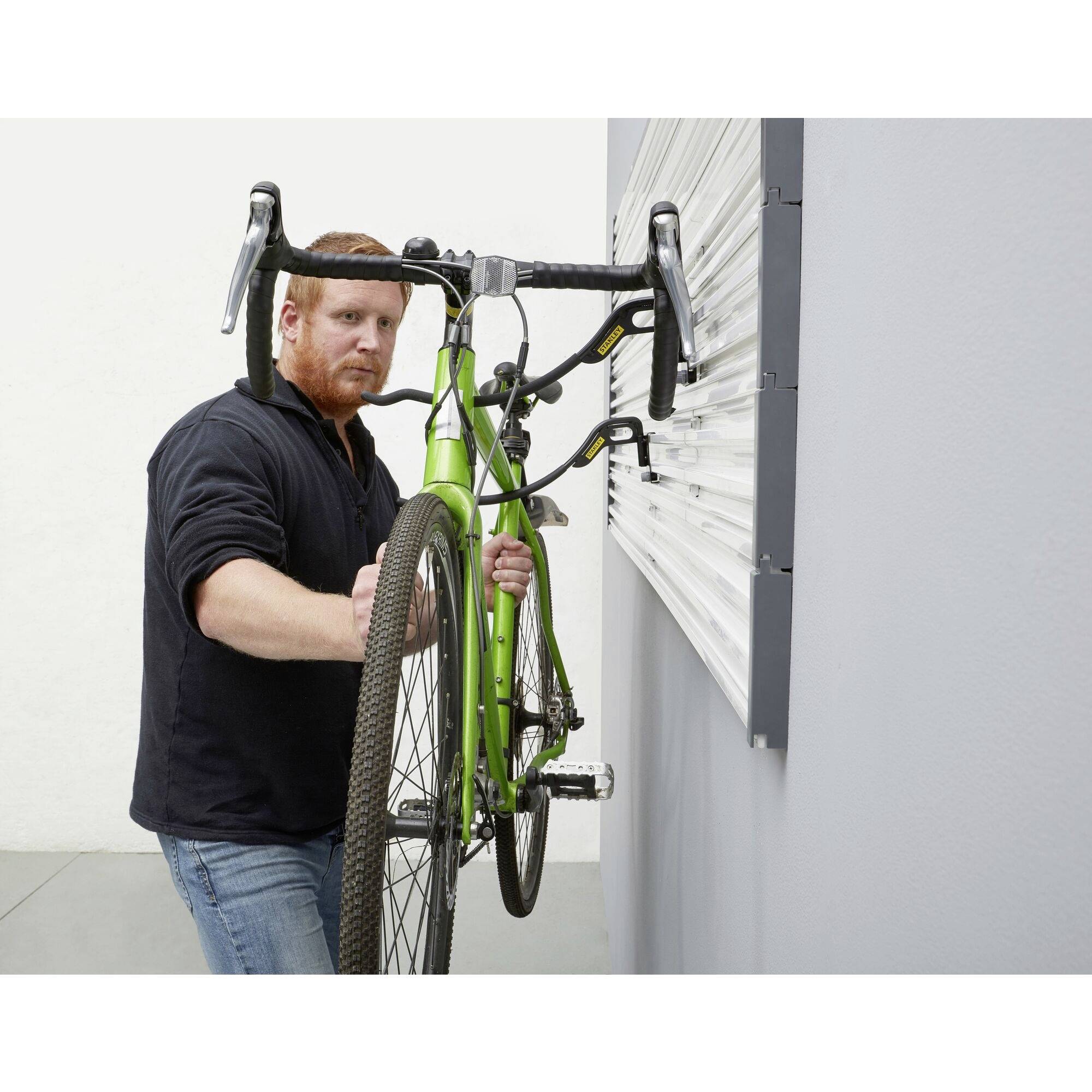 A person is hanging a green bicycle on a wall mount inside a grey wall.