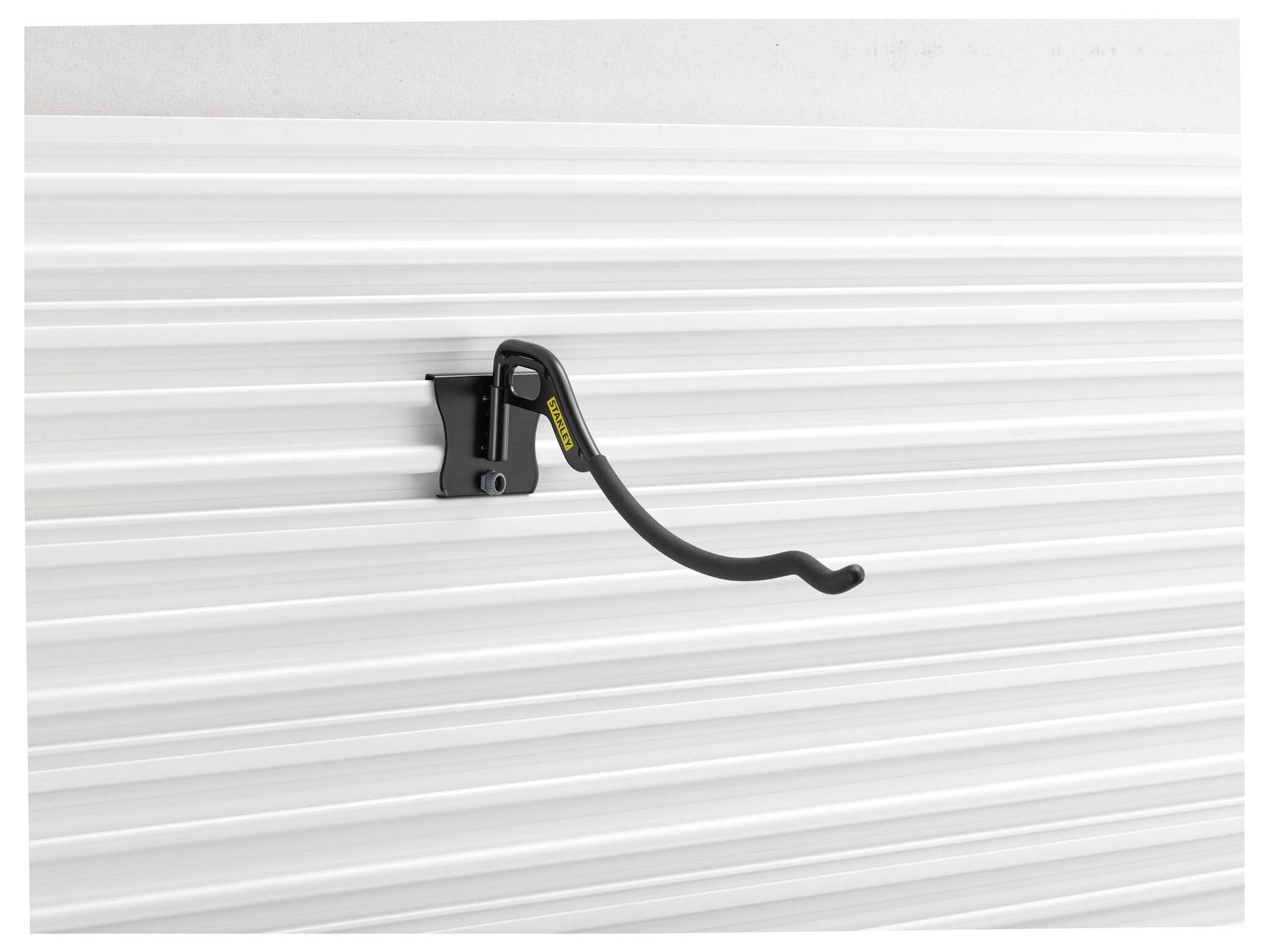A black, curved hook hangs on a white, ribbed wall.