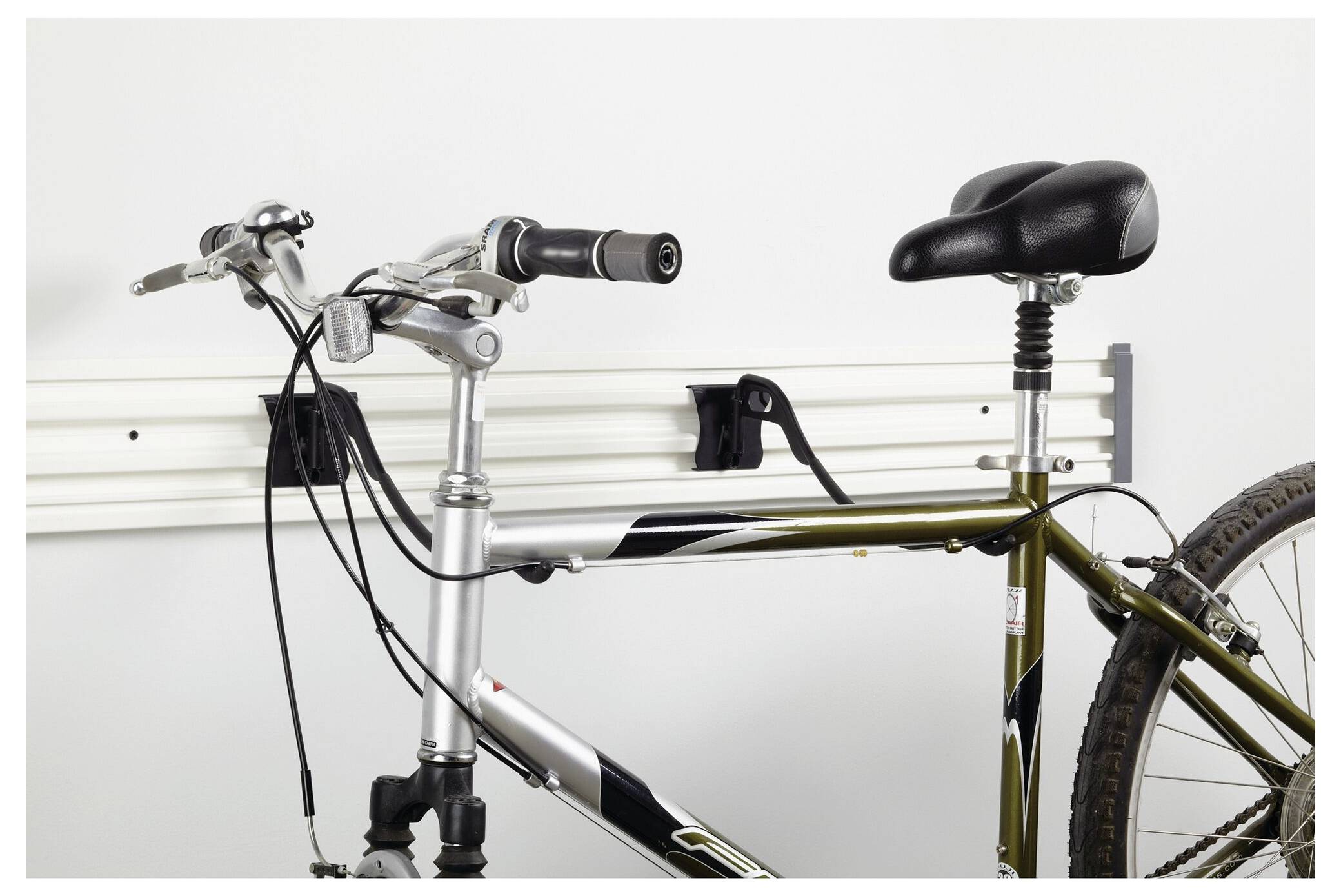 A bicycle hangs on a white wall mount. The front wheel is missing, and the focus is on the frame and handlebars.