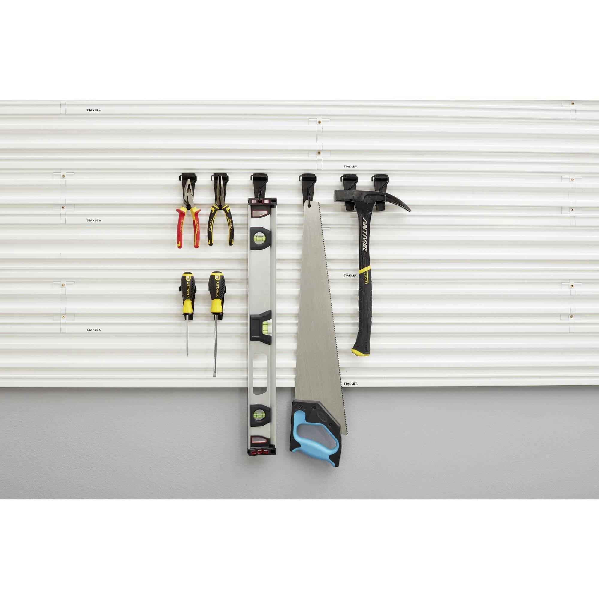 Tools hang on a ribbed wall board: two screwdrivers, three pliers, a spirit level, a saw and a hammer.