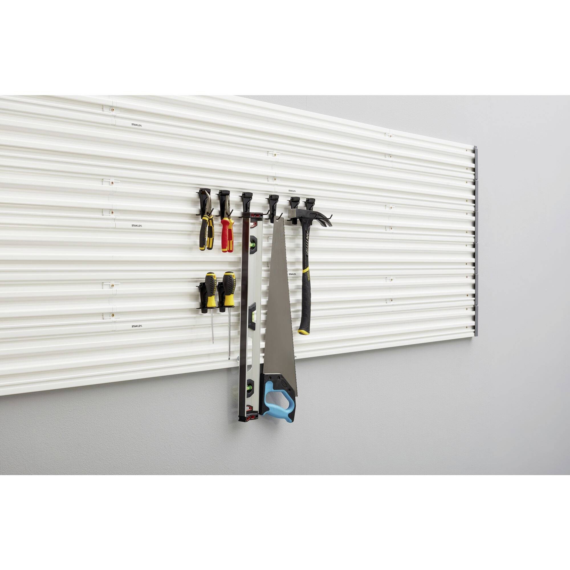 Tool wall with hooks, on which screwdrivers, pliers and a handsaw are hanging; organised and clearly arranged.