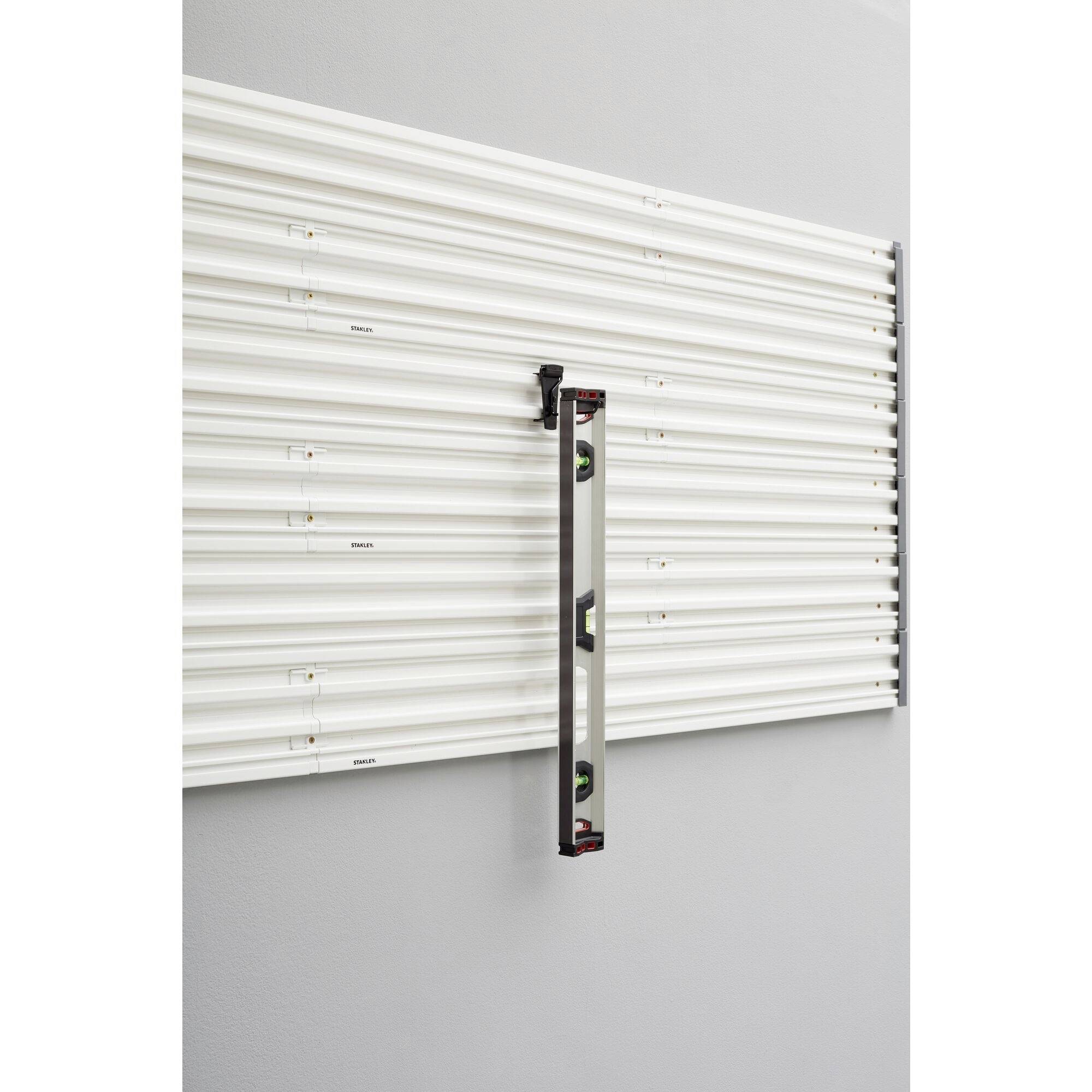 A spirit level hangs vertically on a ribbed, white wall mounting plate.