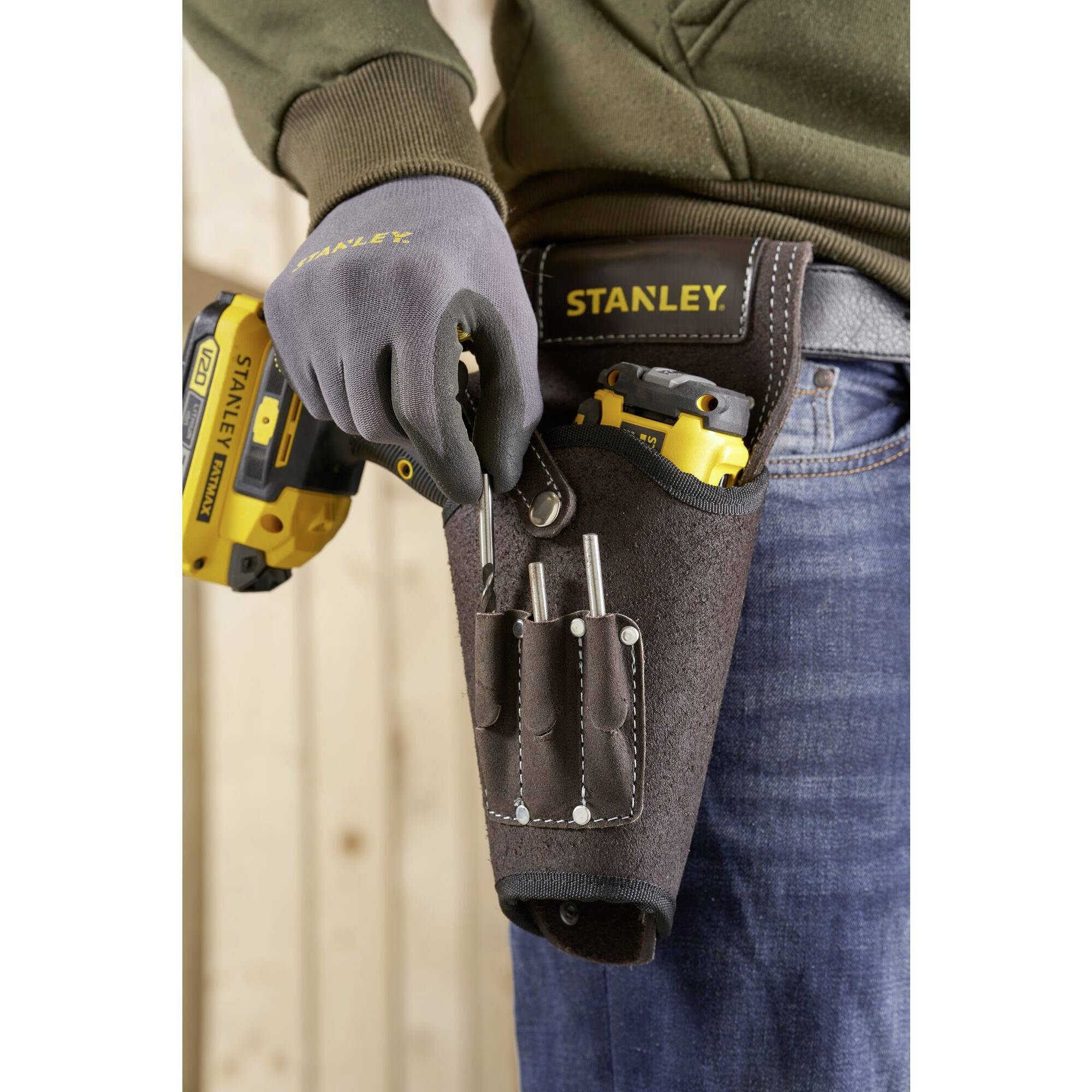 A person is wearing a Stanley tool belt with screwdrivers and a yellow cordless drill in a wood-panelled room.