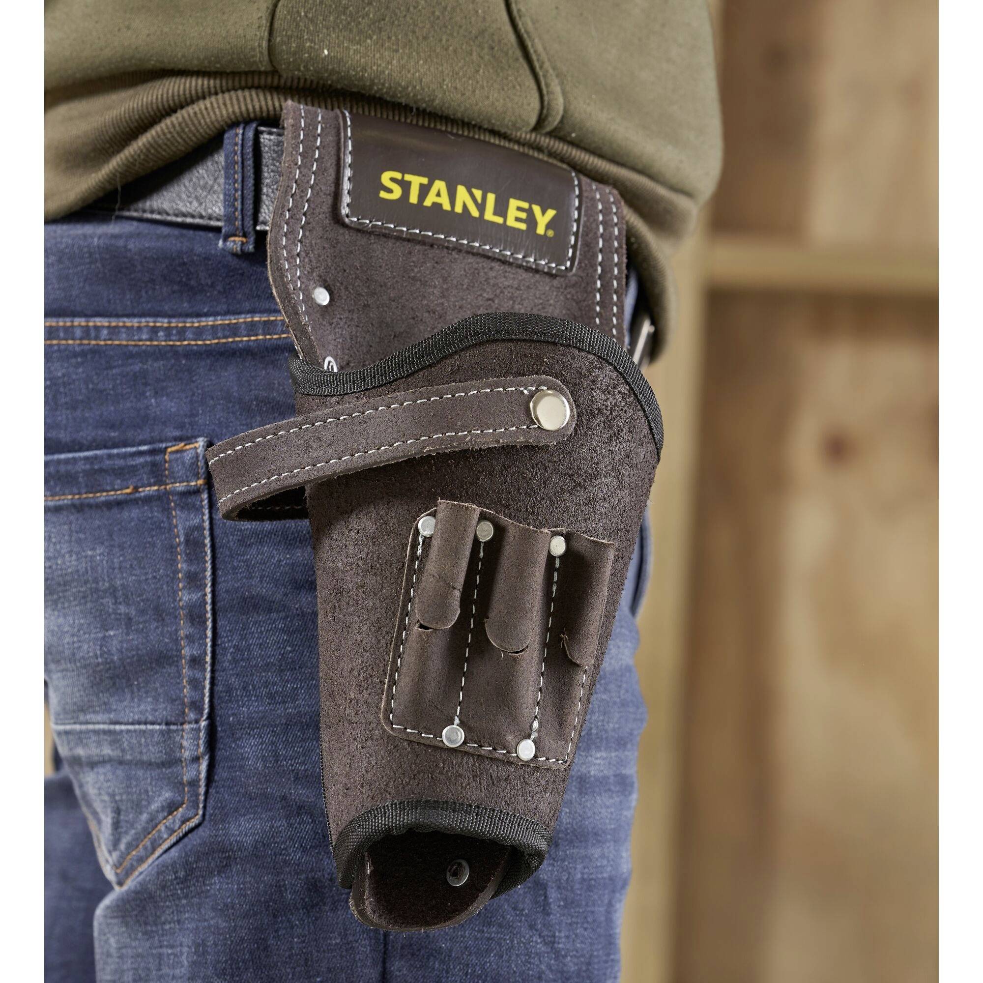 A person is wearing a brown leather tool belt with the 'STANLEY' logo, attached to a belt. It contains multiple compartments.