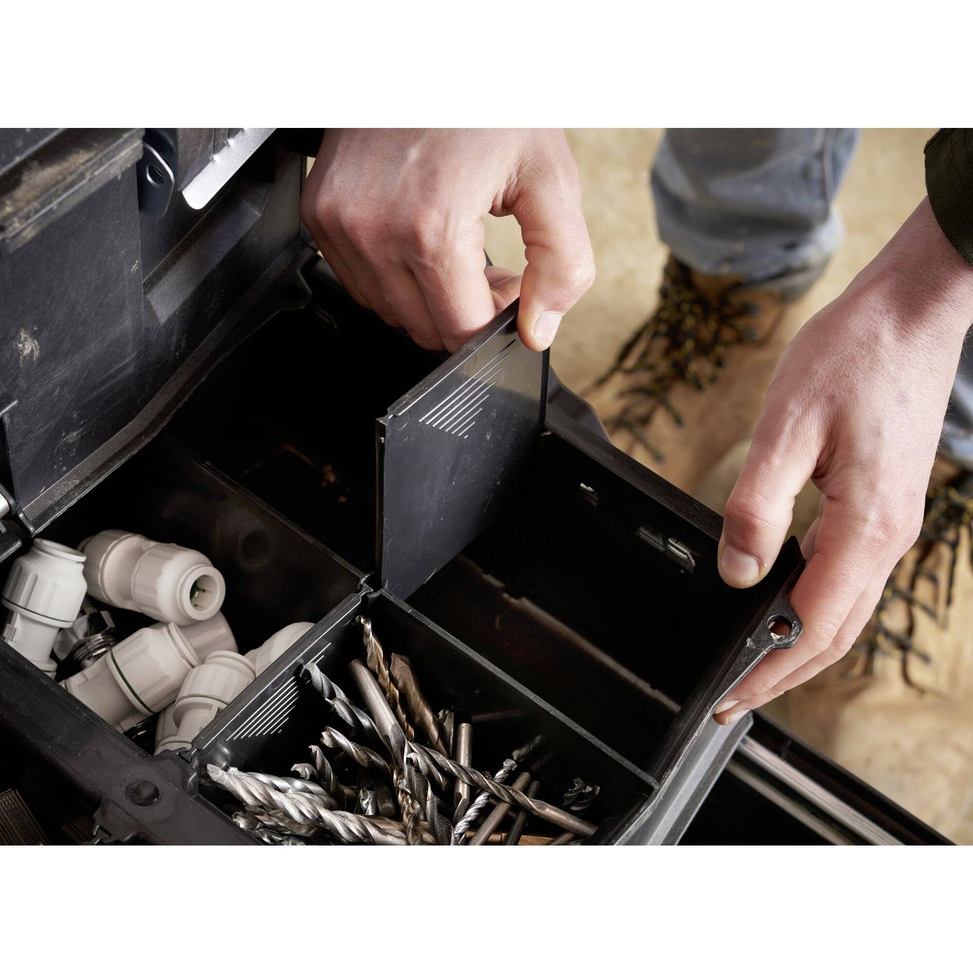 A person is organising a toolbox with drill bits and cable connections. Hands are reaching for a small tool in the compartment.