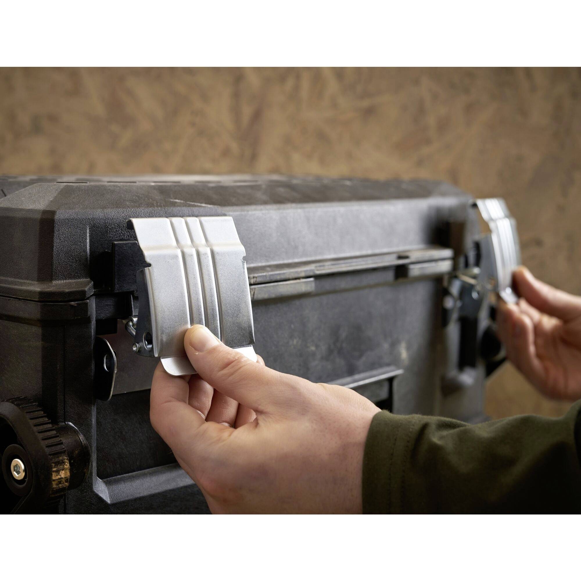 A person is closing a black toolbox with metal latches. The surrounding environment is blurred, with the focus on the latches.