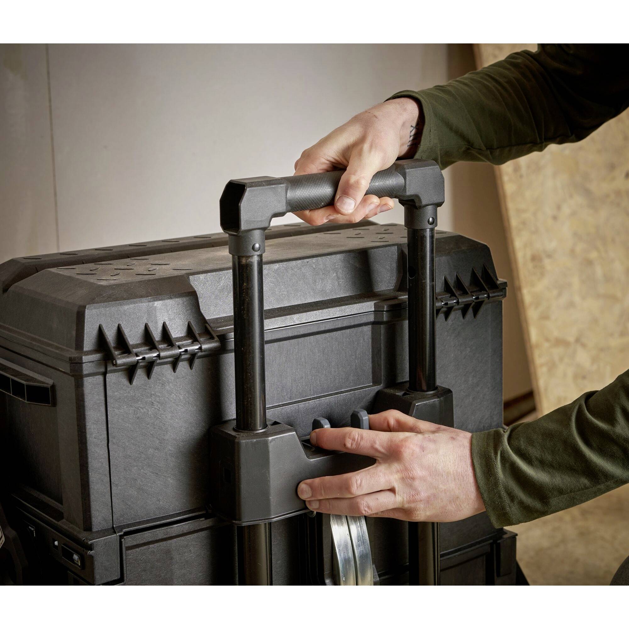 A person is pulling a black tool case with an extendable handle across a light-coloured surface.