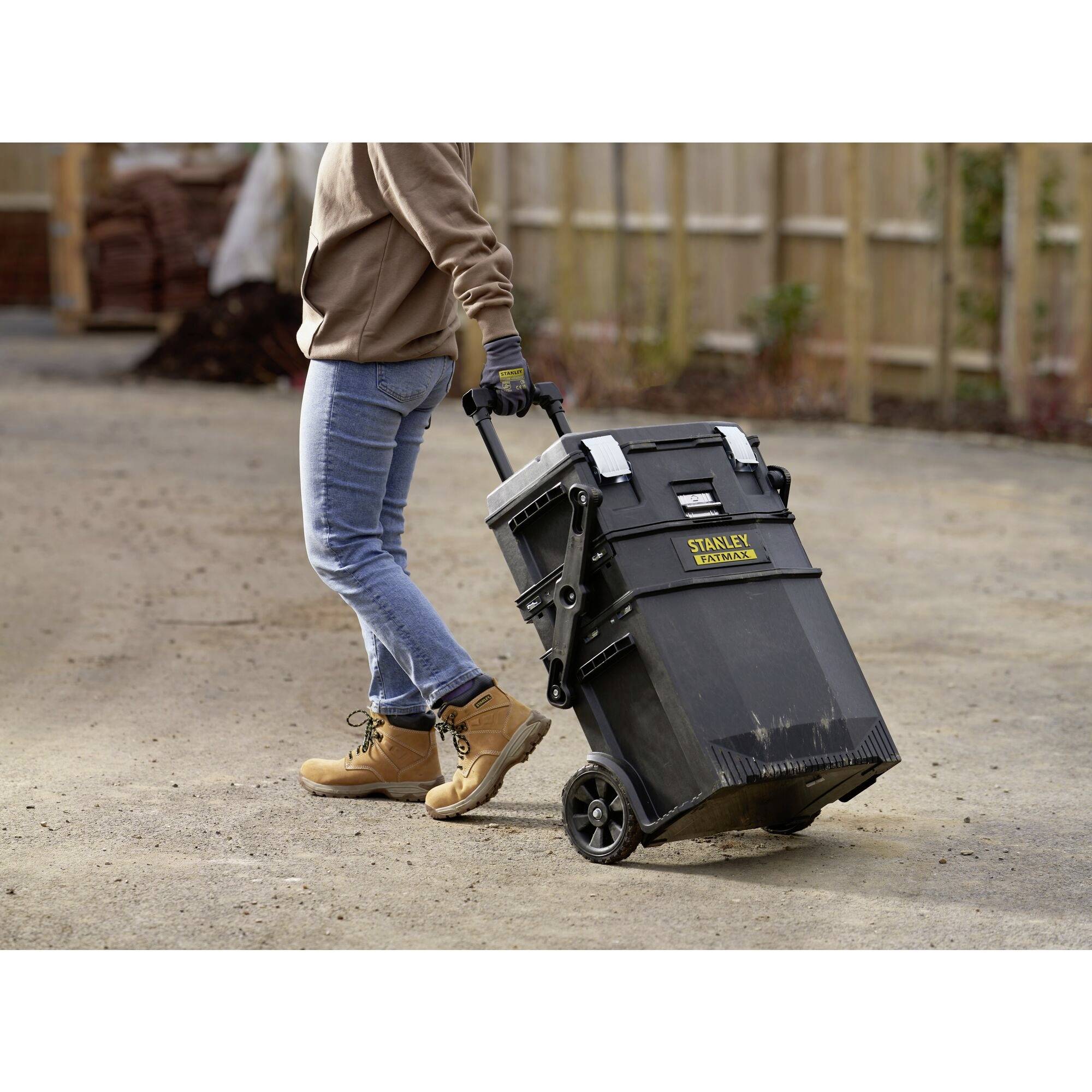 A person is pulling a black wheeled toolbox across a concrete floor. The box bears the 'Stanley Fatmax' logo.
