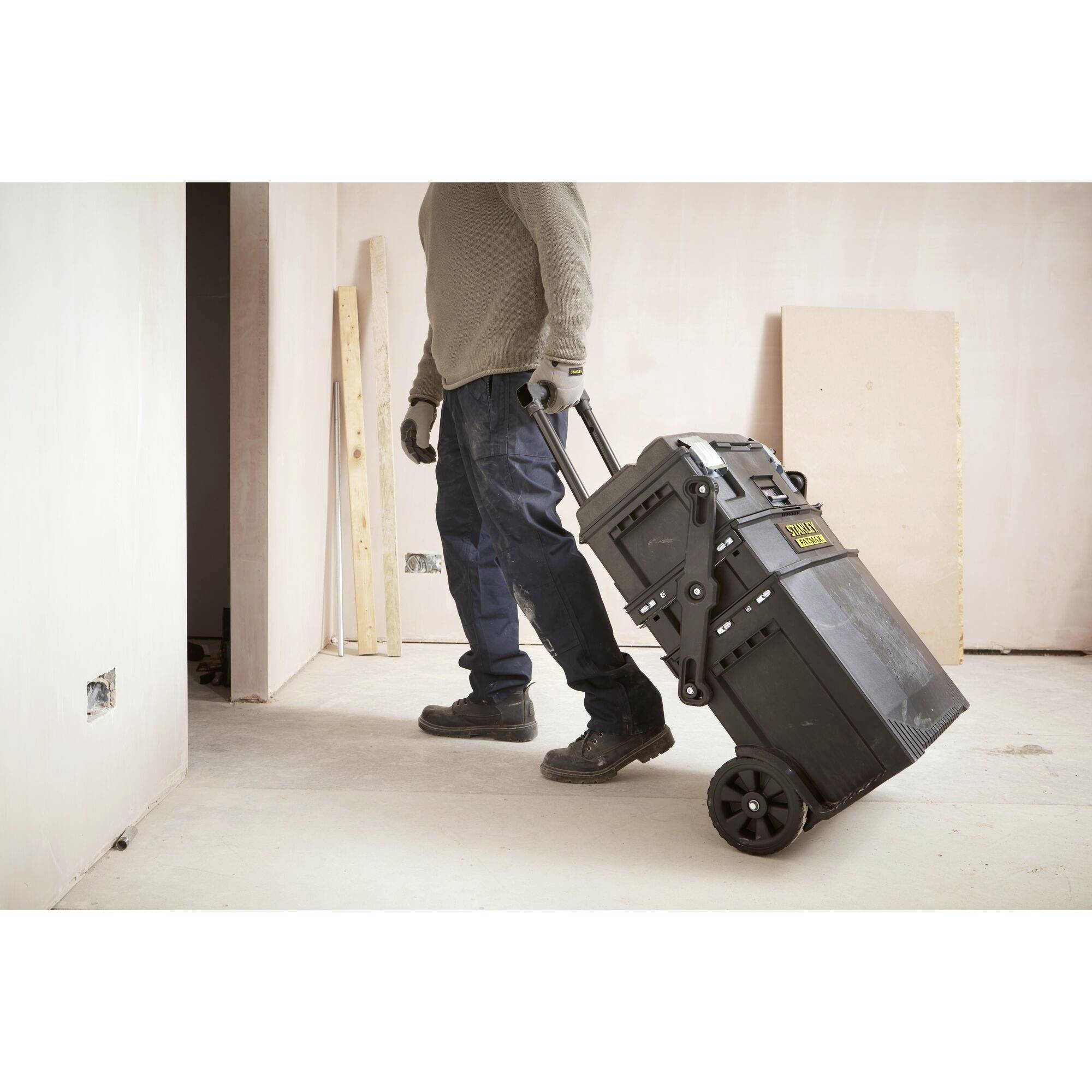 A person is pulling a black, mobile toolbox with wheels across a room on a building site.