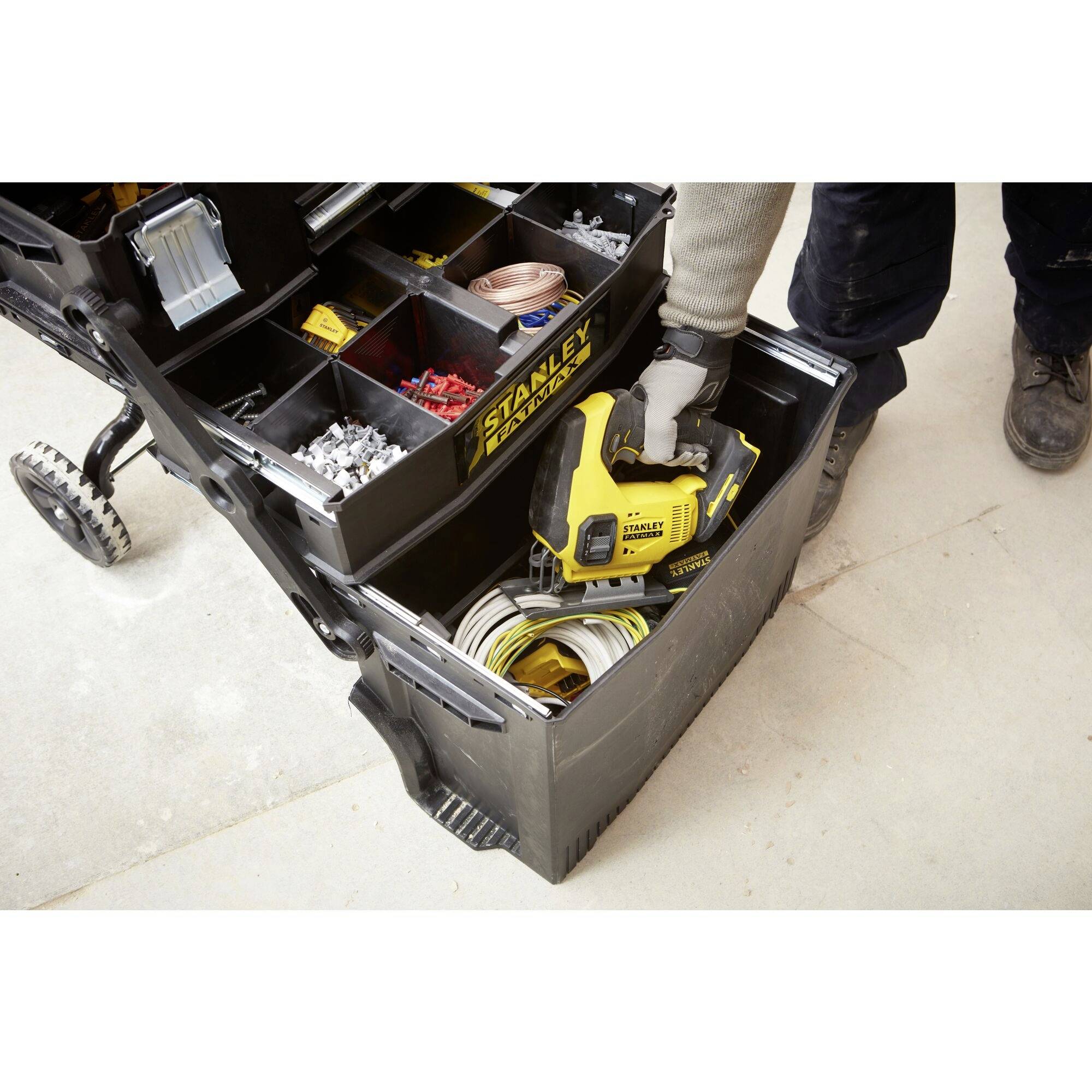 A person is retrieving a yellow electrical device from a compartment trolley with many sections filled with tools and accessories.