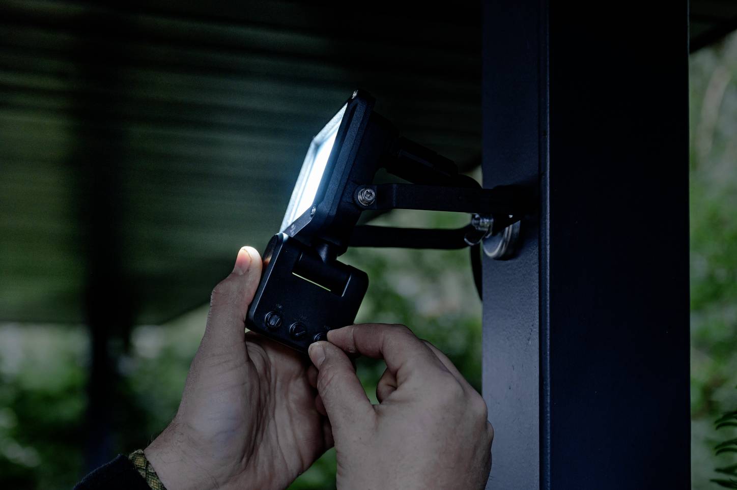 A person is adjusting an illuminated device mounted on a black metal pole in a dimly lit environment.