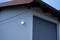 An illuminated exterior light on a building casts light on the white wall and grey garage door during twilight.