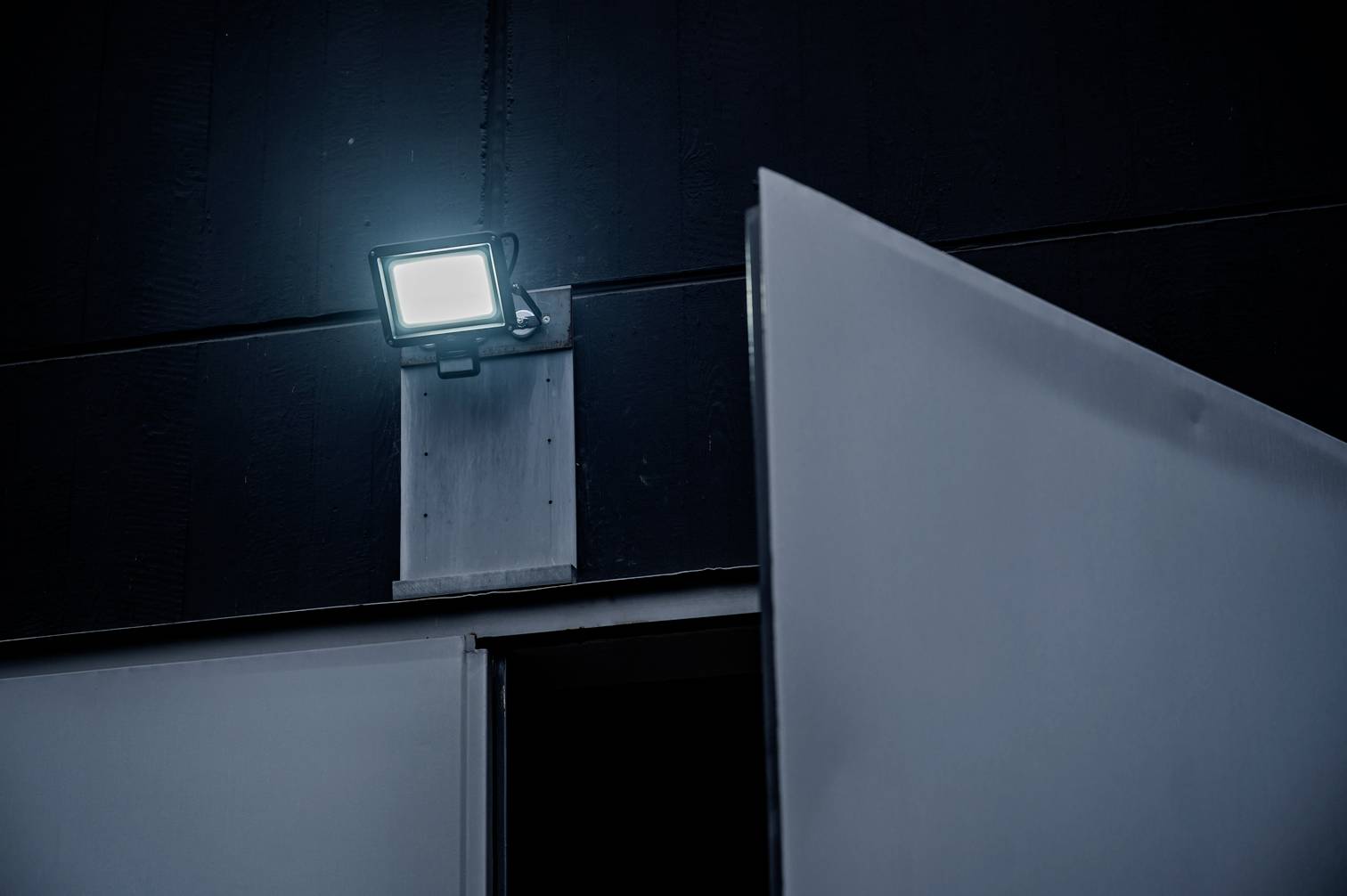 An open door in a dark room is illuminated by a bright external spotlight.