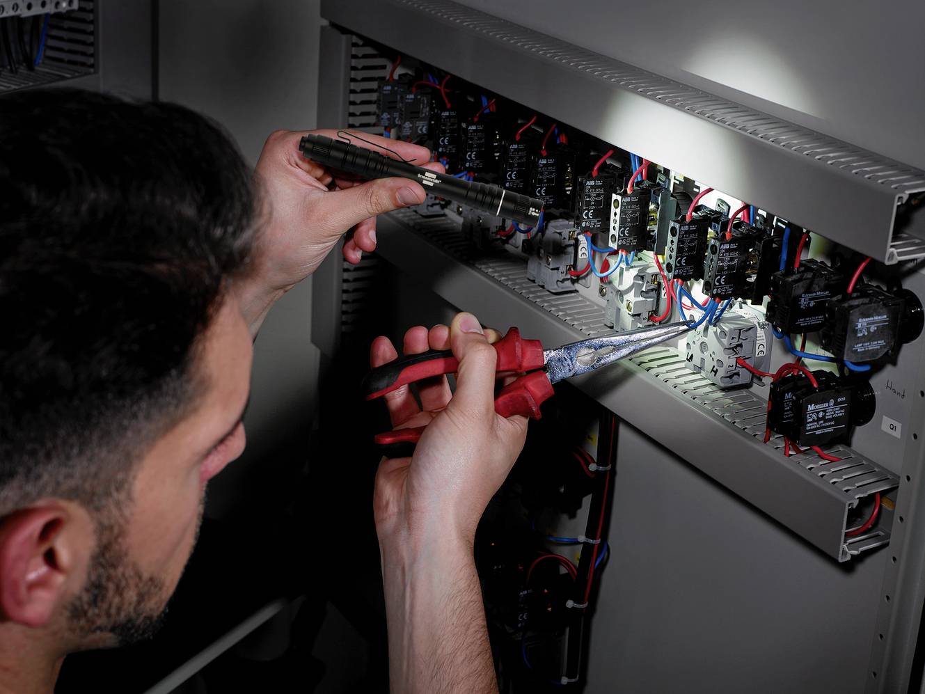 A person is working on an electrical control panel and using a screwdriver and pliers to secure cables.