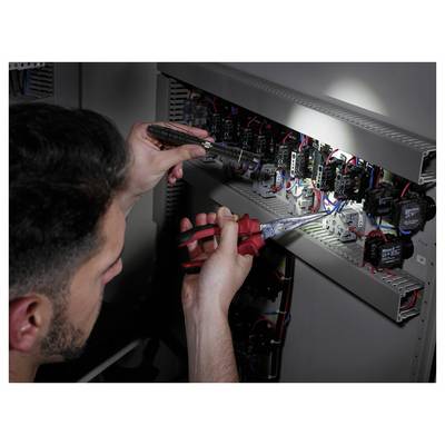 Technician wiring and inspecting an electrical control panel with a screwdriver and pliers, surrounded by relays, switches, and cables.<br>