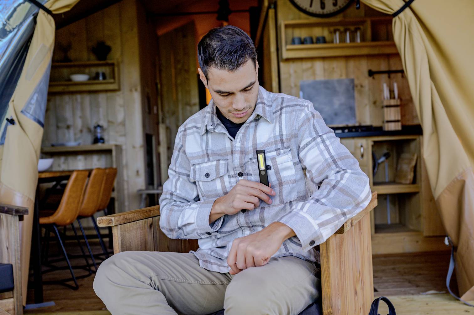 A man is sitting in a wood-panelled room and is placing a USB stick in his shirt pocket. A kitchen can be seen in the background.