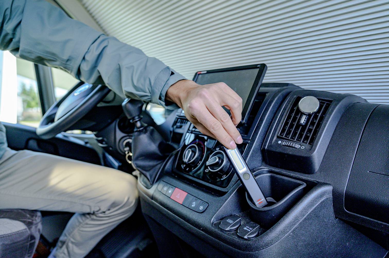 A person inserts a key into the ignition of a vehicle. The cockpit is modern with a digital display.